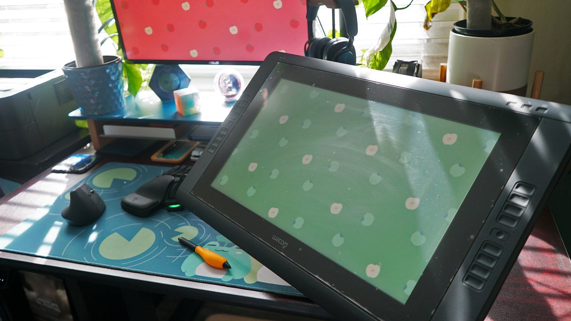  A brightly lit workspace featuring a graphic tablet and stylus, ergonomic mouse, and a monitor with a colourful background, surrounded by indoor plants