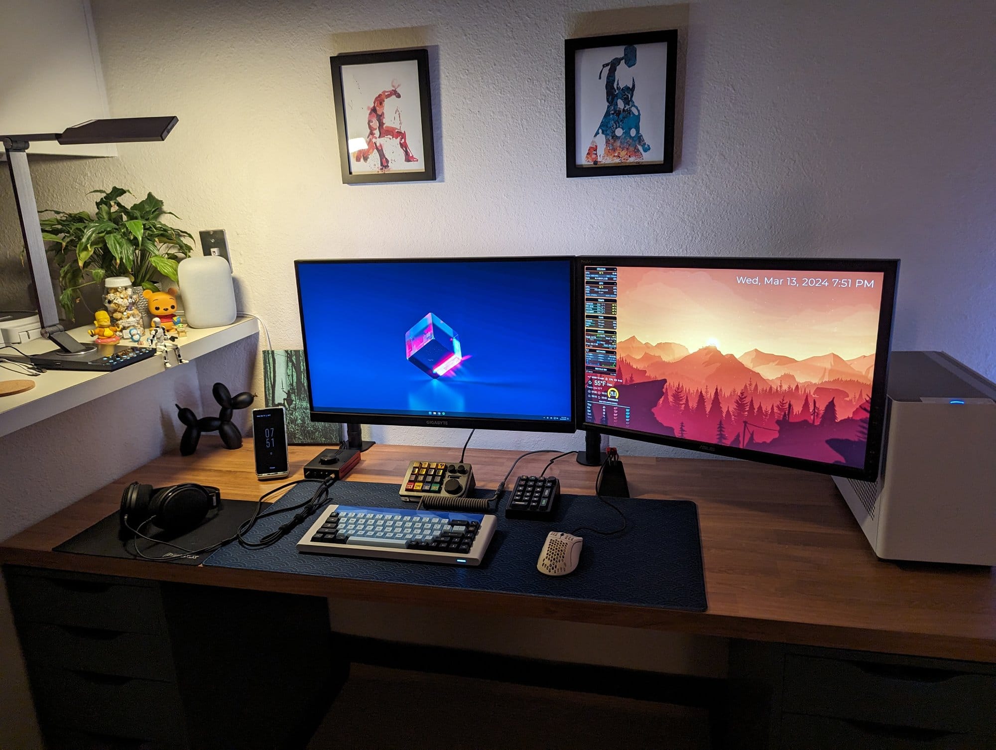 An organised desk with a computer sporting dual monitors with colorful wallpapers, a mechanical keyboard, headphones, and a shelf with plants and figurines, all under warm ambient lighting