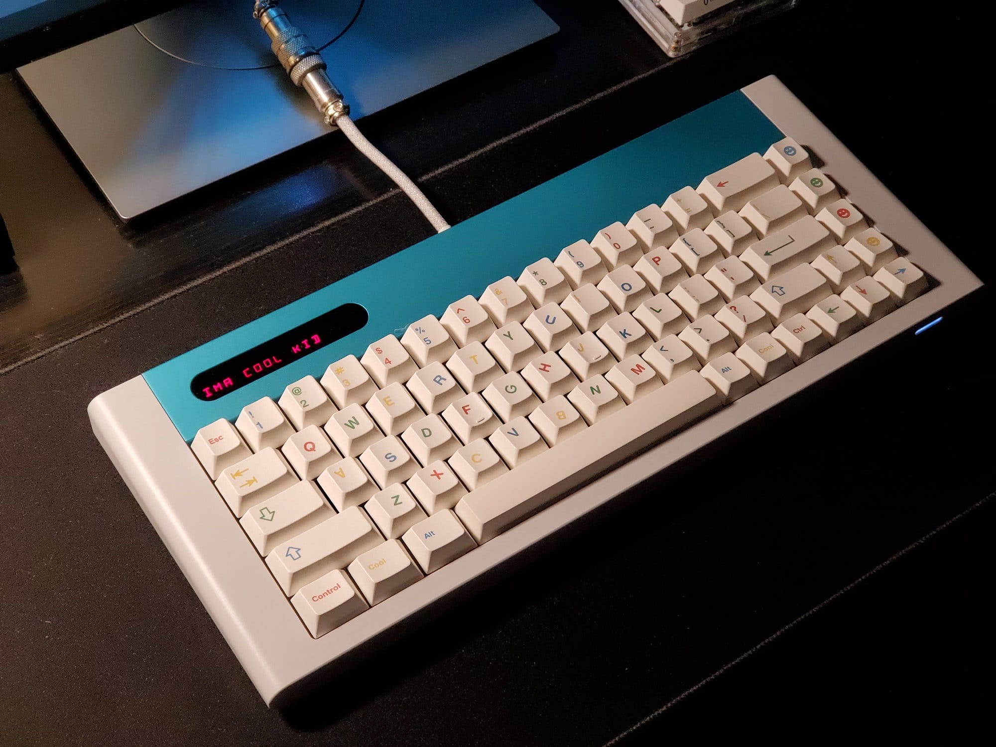 A close-up of a custom mechanical keyboard with white and pastel-coloured keycaps on a dark desk surface