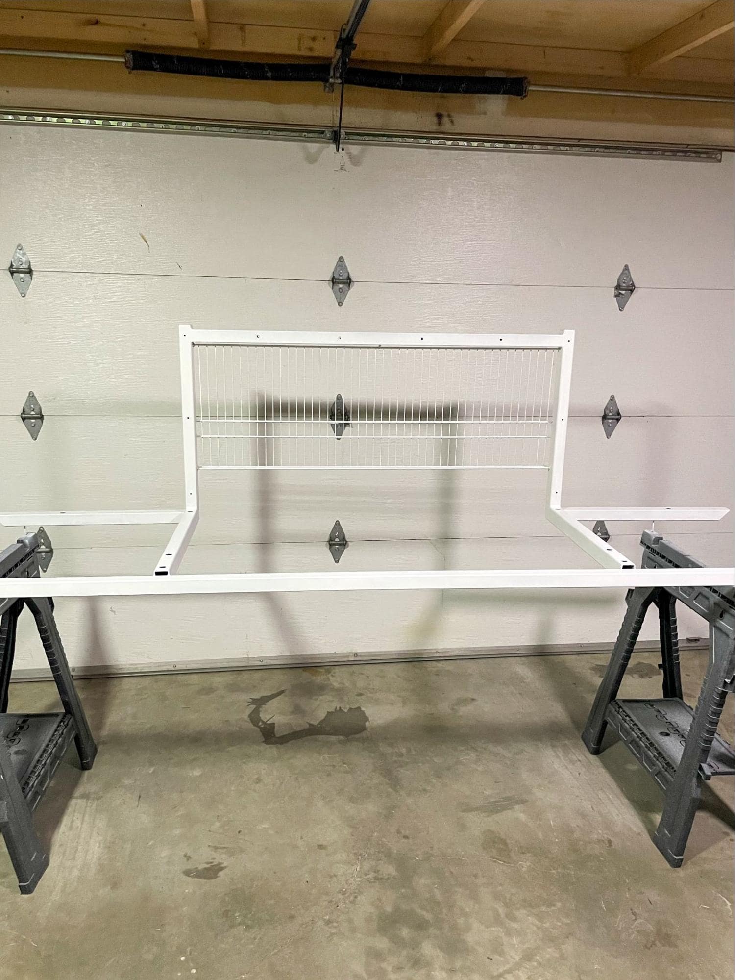 A partially constructed white floating desk supported by sawhorses in a garage, with a concrete floor and garage door track visible overhead