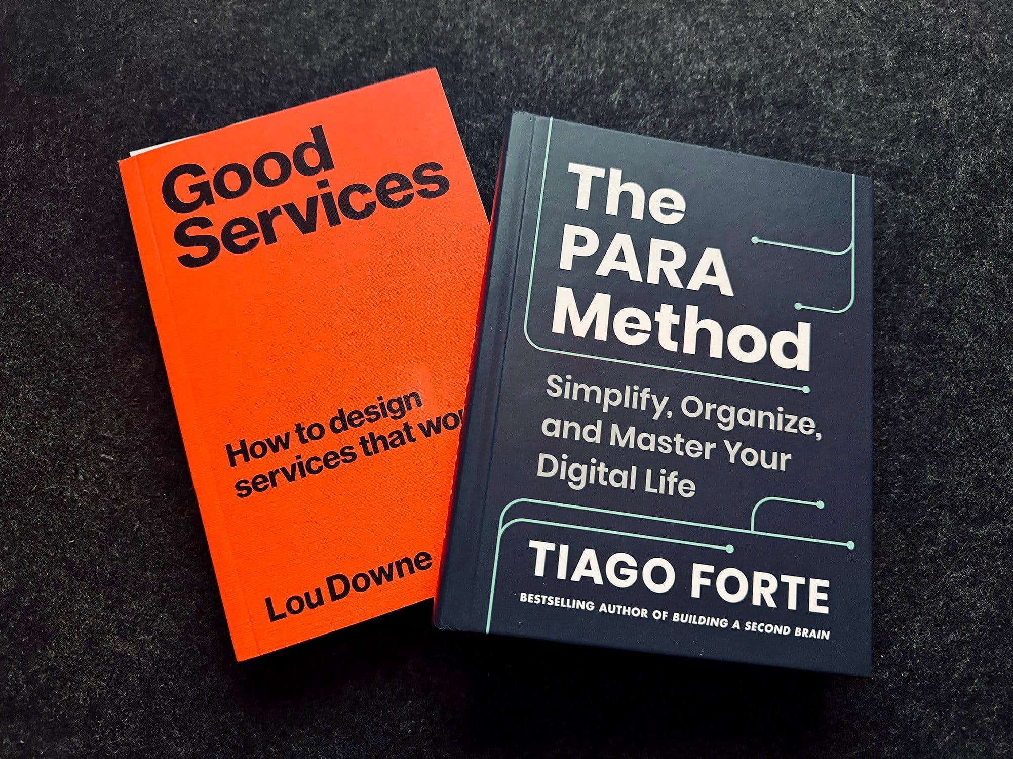  Two books titled “Good Services: How to design services that work” by Lou Downe and “The PARA Method: Simplify, Organize, and Master Your Digital Life” by Tiago Forte, lying on a dark surface