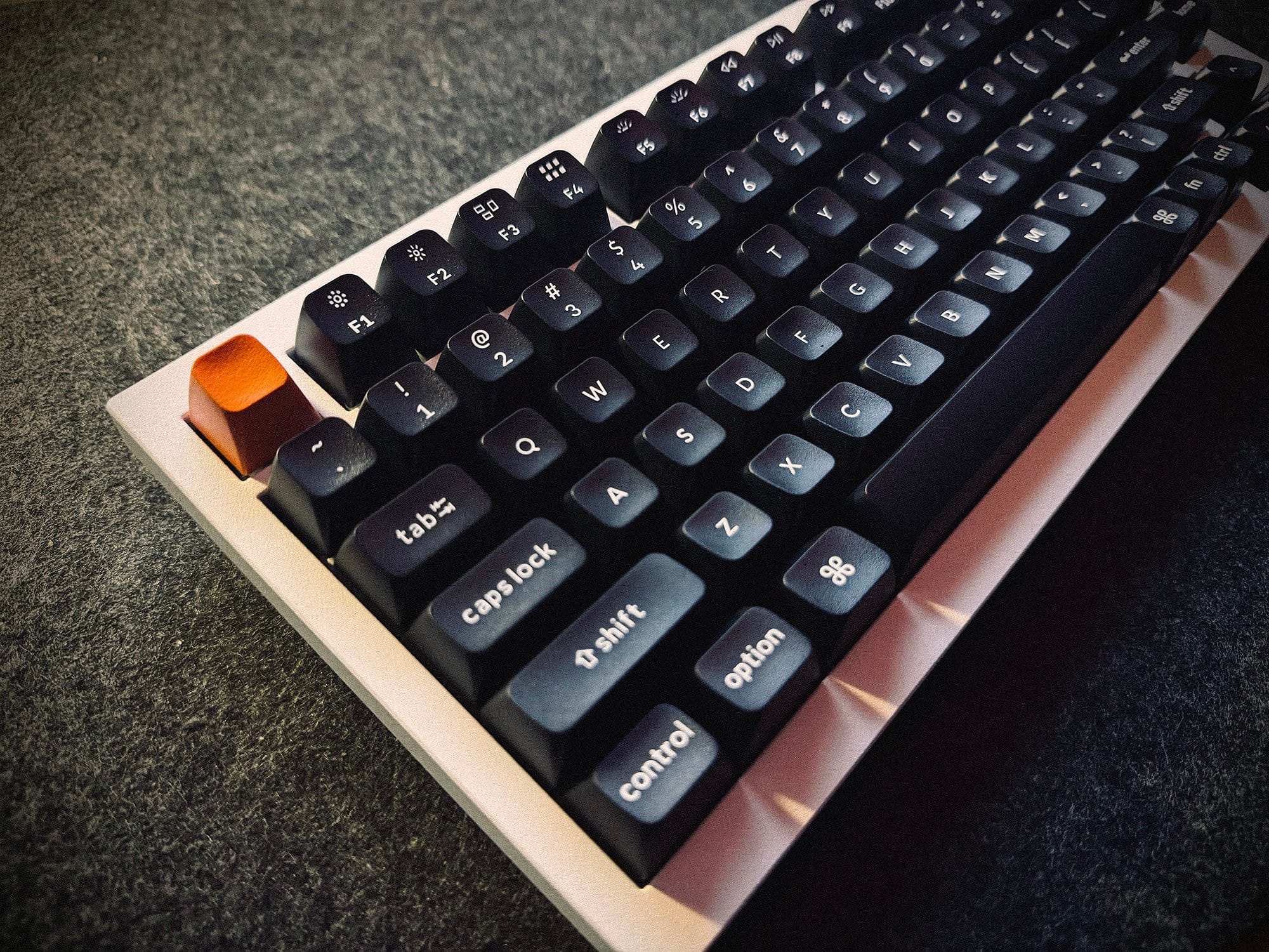 An angled view of a mechanical keyboard with black keys and a distinctive orange escape key