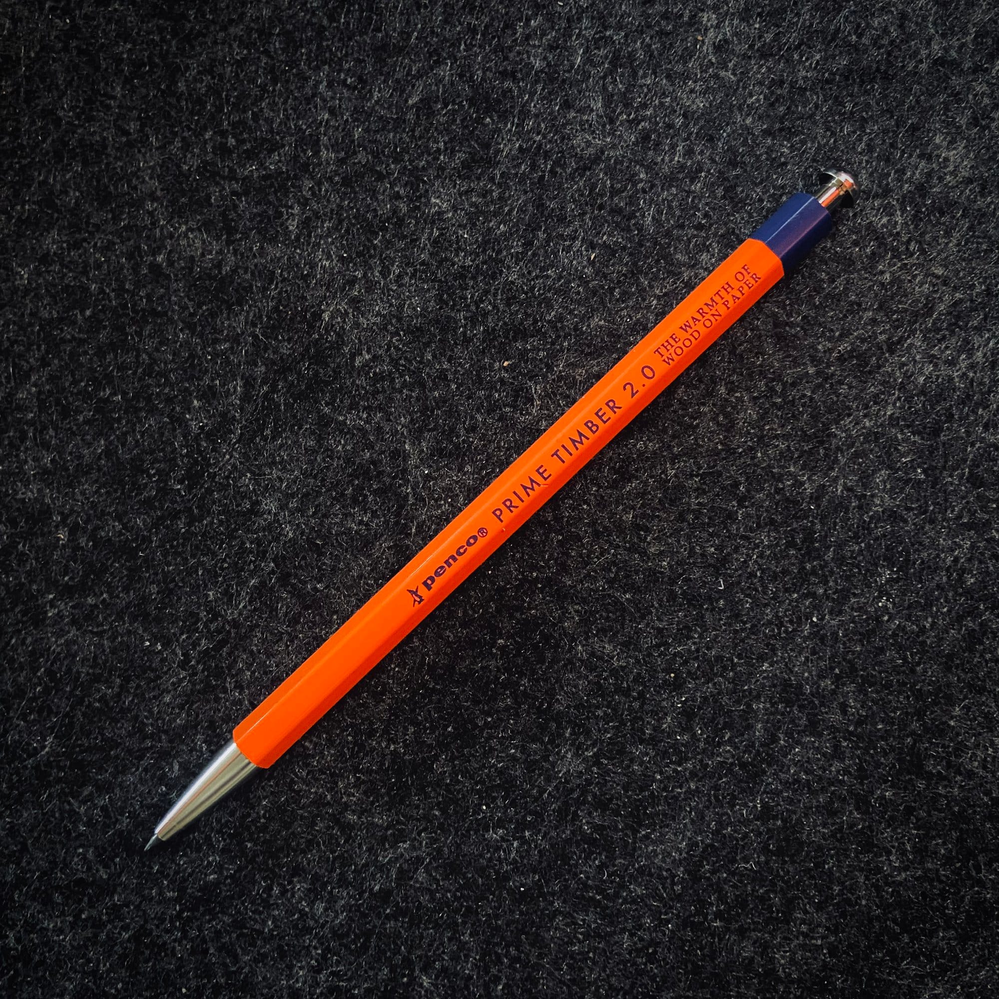 An orange mechanical pencil with text labelling it as “Prime Timber 2.0“ resting on a dark felt surface