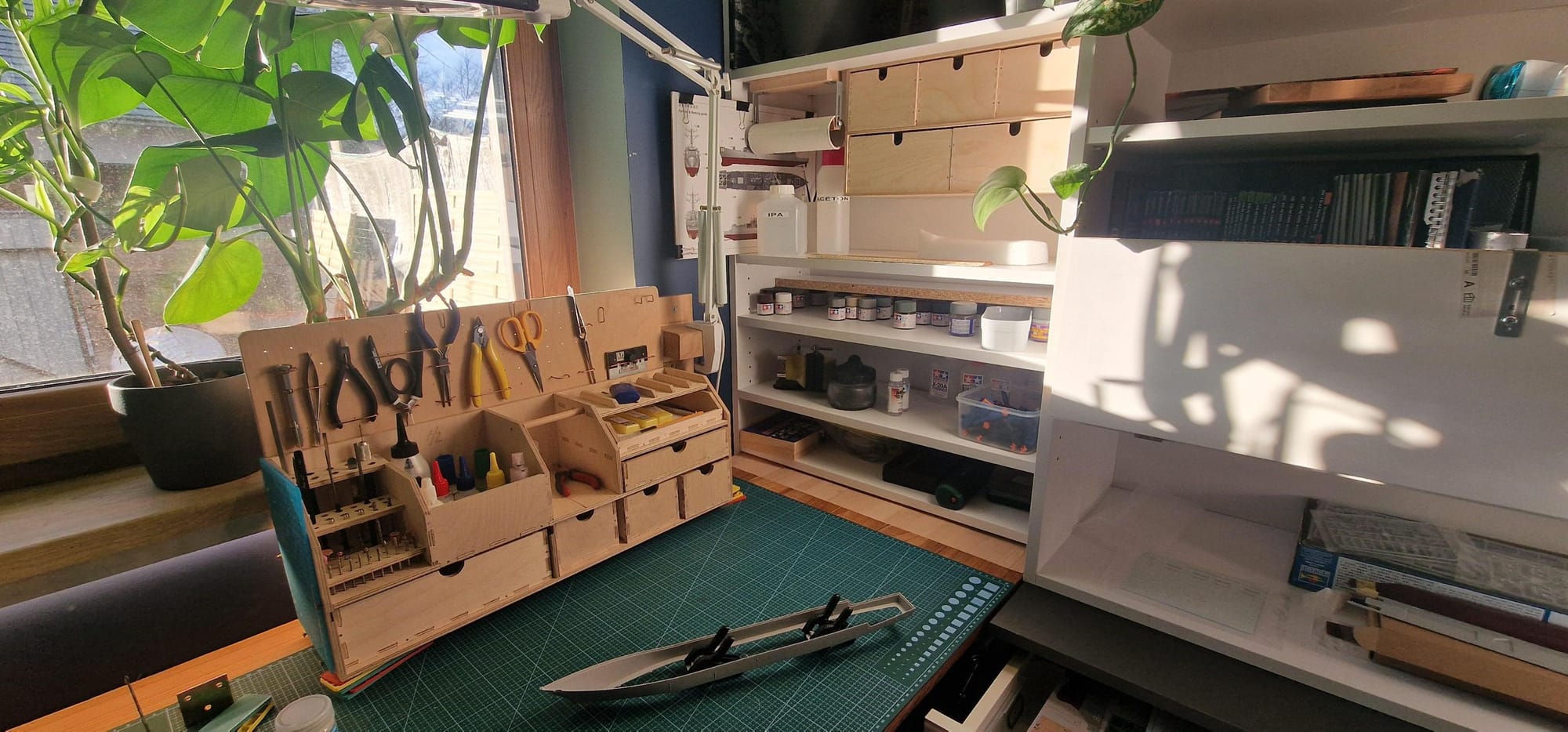 A detailed and organised crafting area illuminated by natural sunlight, featuring a well-equipped tool organiser and shelving stocked with various art supplies