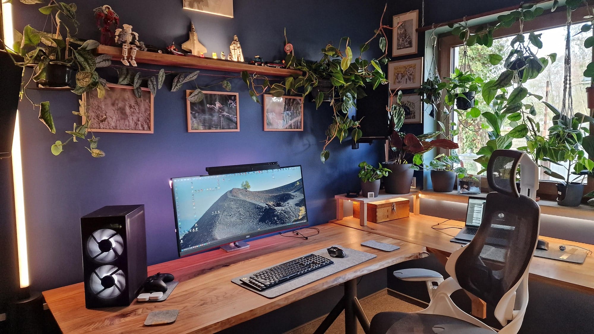 A spacious and modern home office adorned with lush green plants and featuring a large desk with a gaming monitor, ergonomic chair, and atmospheric lighting