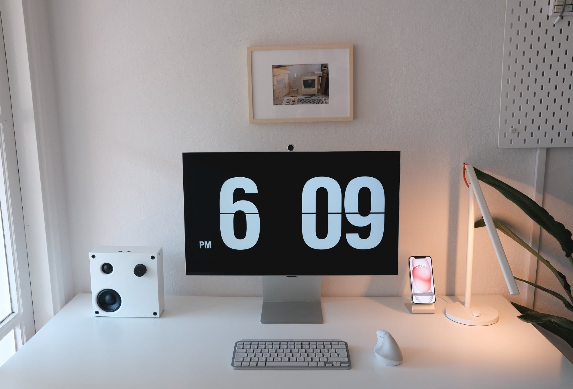 A white desk setup featuring a Samsung Viewfinity S9 monitor, Logitech MX Keys Mini Mac keyboard, Logitech Lift mouse, IKEA VAPPEBY speaker, and an iPhone on a stand
