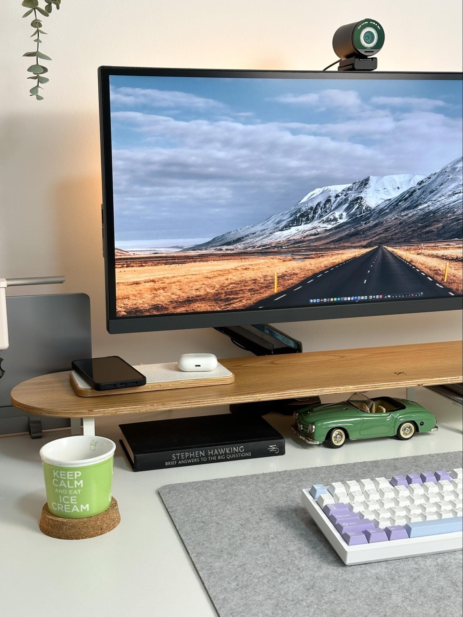 A workspace with a BenQ PD3420Q UltraWide monitor, an EMEET webcam, an Epomaker Ajazz AK820 keyboard on a felt mat, a Woodcessories desk shelf, a MacBook laptop stand, a green toy car, a book by Stephen Hawking, and a mug with the text that reads “KEEP CALM AND EAT ICE CREAM”