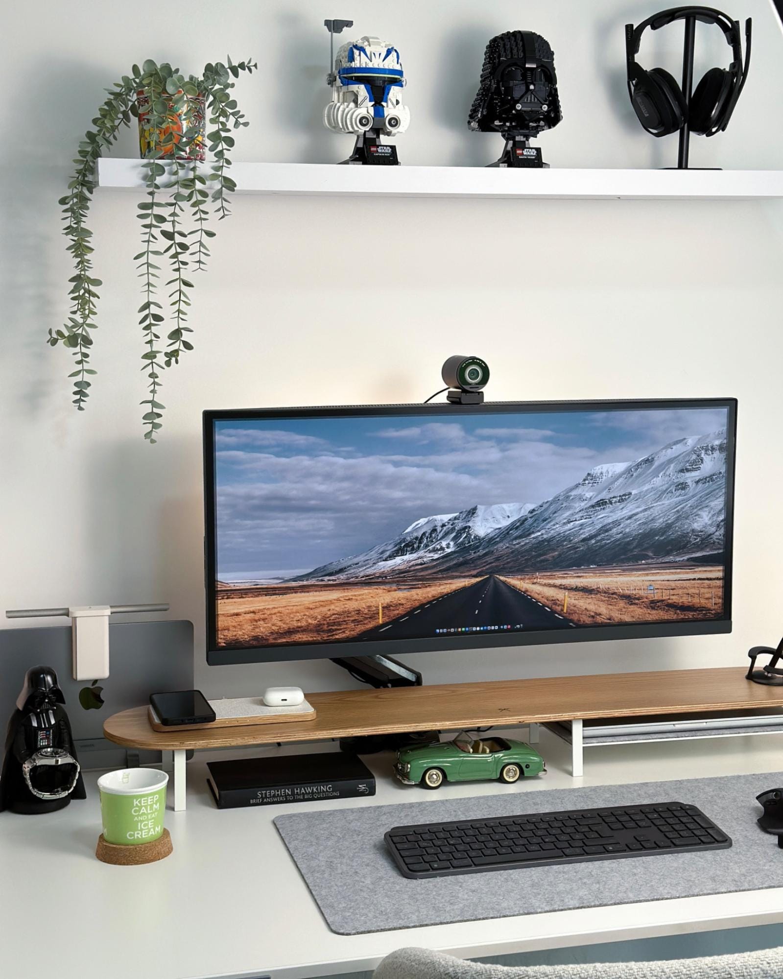A desk setup featuring a BenQ widescreen monitor with an EMEET webcam, a Logitech MX keyboard, a Logitech MX Master 3S mouse on a felt mat, a Woodcessories desk shelf, and LEGO Star Wars Darth Vader and Captain Rex helmets on a shelf above, along with an Astro A50 headset