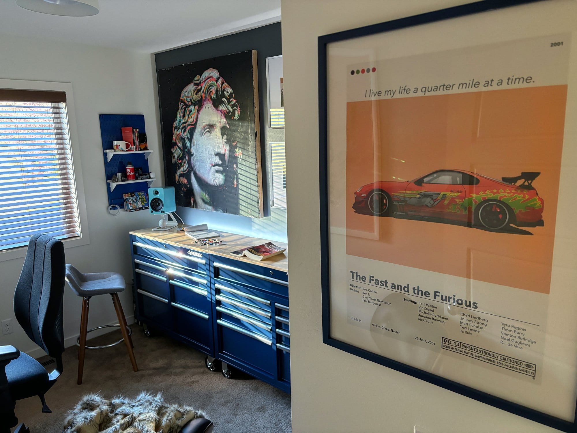 A workspace with a Husky workbench, a Kanto YU4 speaker, a large sculpture print, and a framed The Fast and the Furious poster on the wall