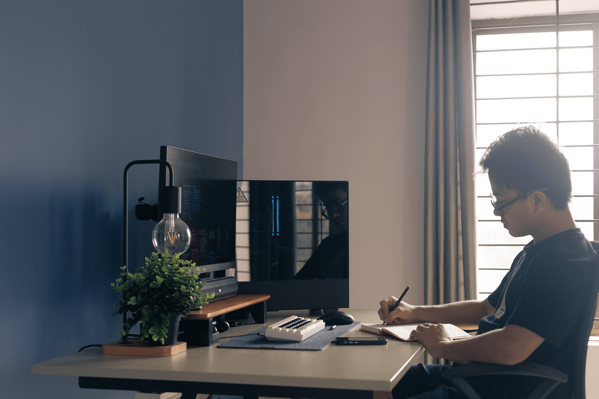 A man working at an IKEA TROTTEN desk with a BenQ PD2500Q monitor and EPOMAKER Skyloong SK61 keyboard