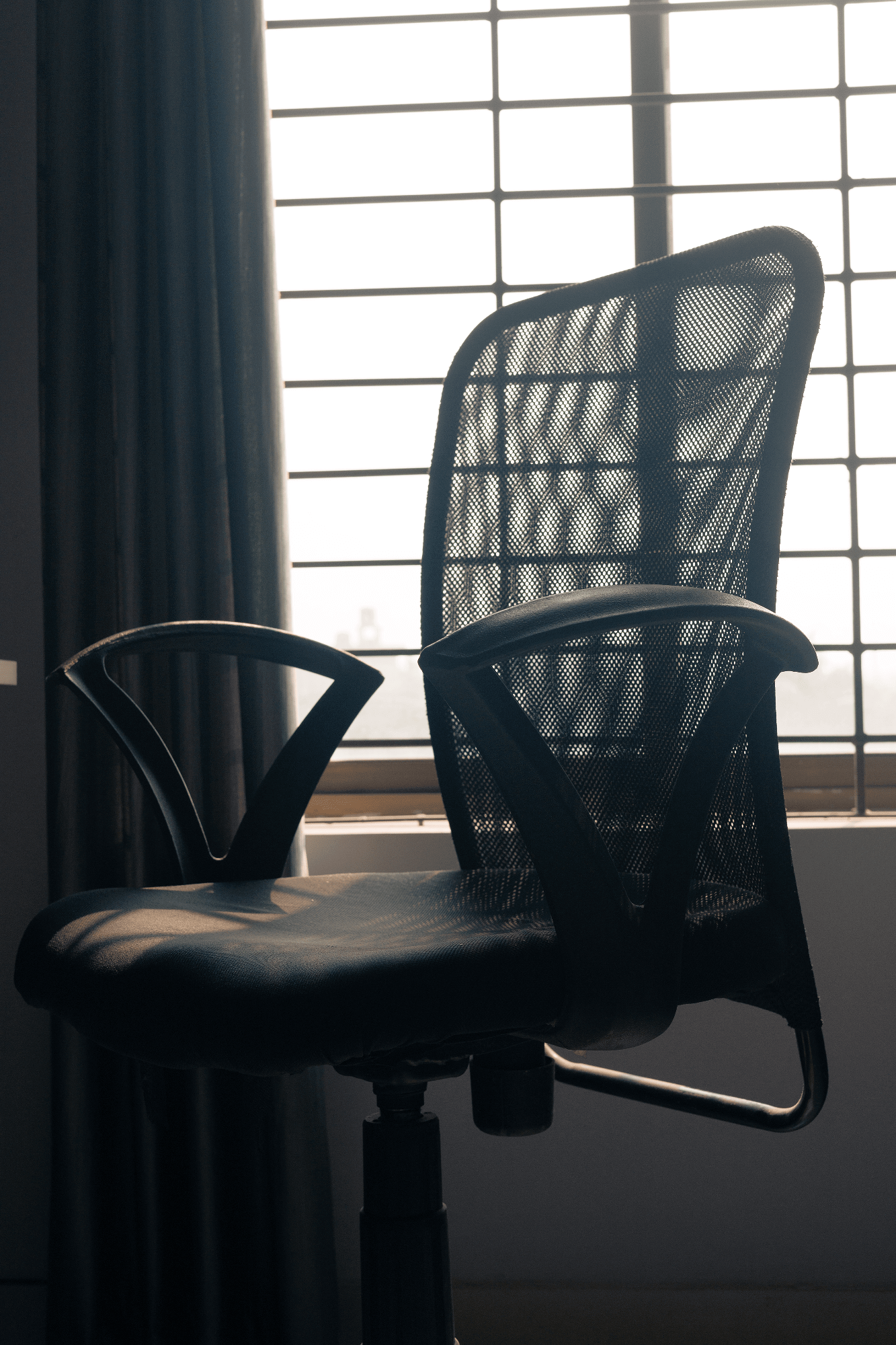 A Greensoul ergonomic chair with a mesh backrest by a window with bars and curtains