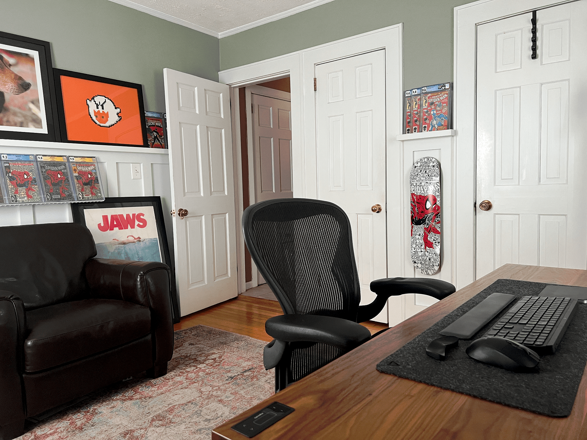 A home office with a Herman Miller Aeron chair, Spider-Man skateboard and framed Jaws poster
