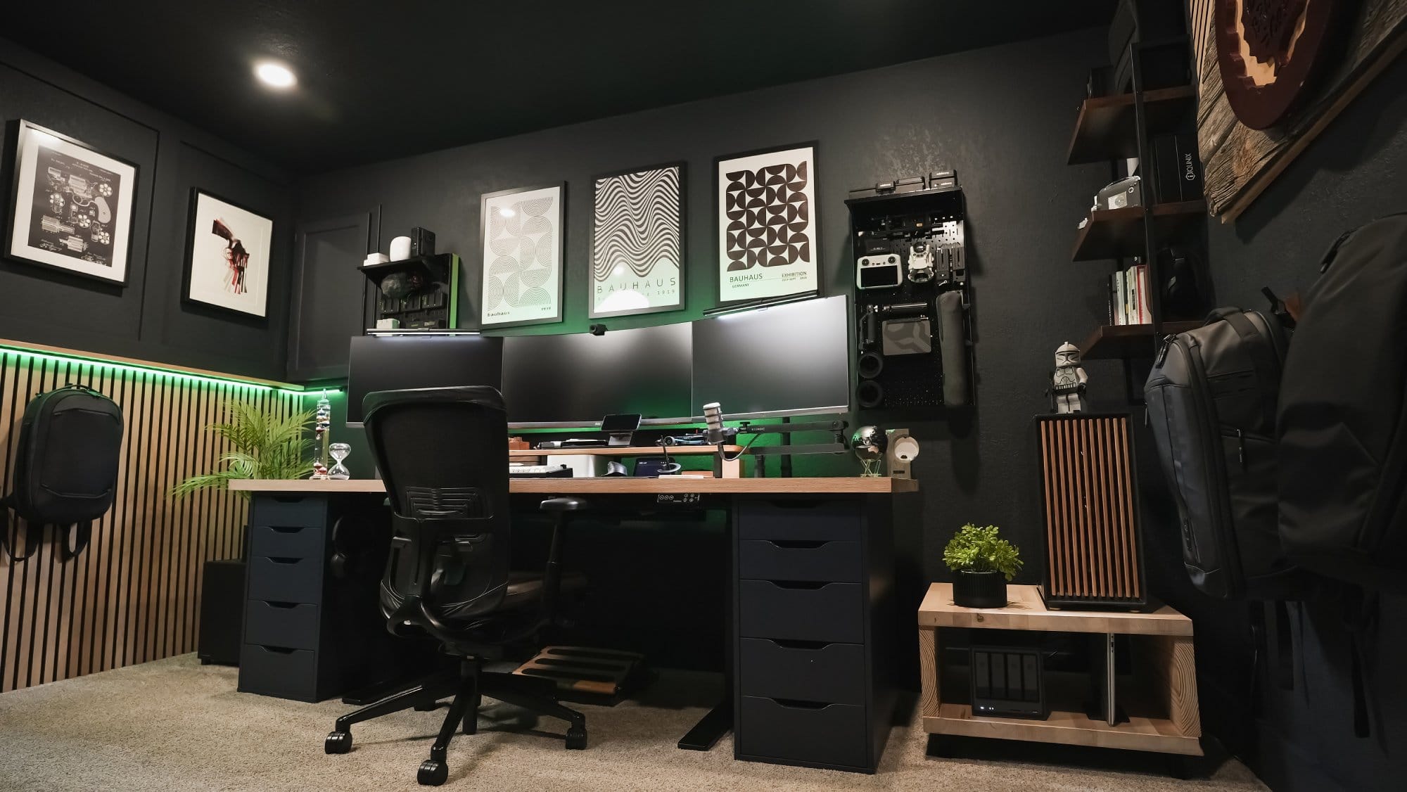 modern home office desk setup with triple monitors, ergonomic chair, custom pc with green lighting, wall mounted gear storage, and minimalist decor