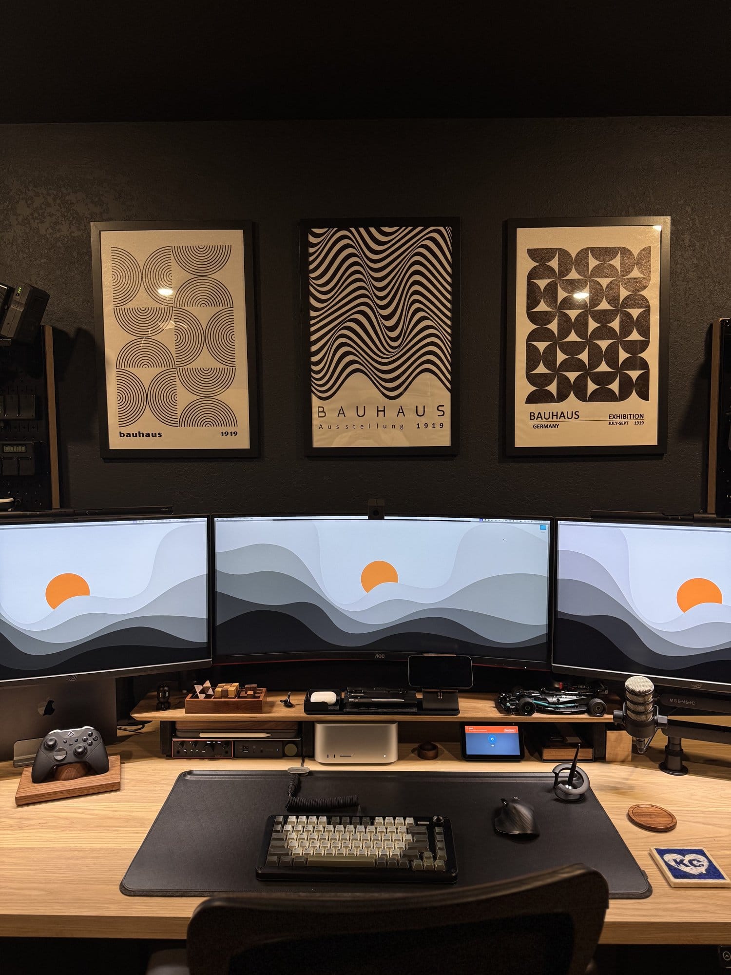 roductivity desk setup with triple curved monitors, custom mechanical keyboard, studio microphone, gaming controller, and minimalist Bauhaus wall art