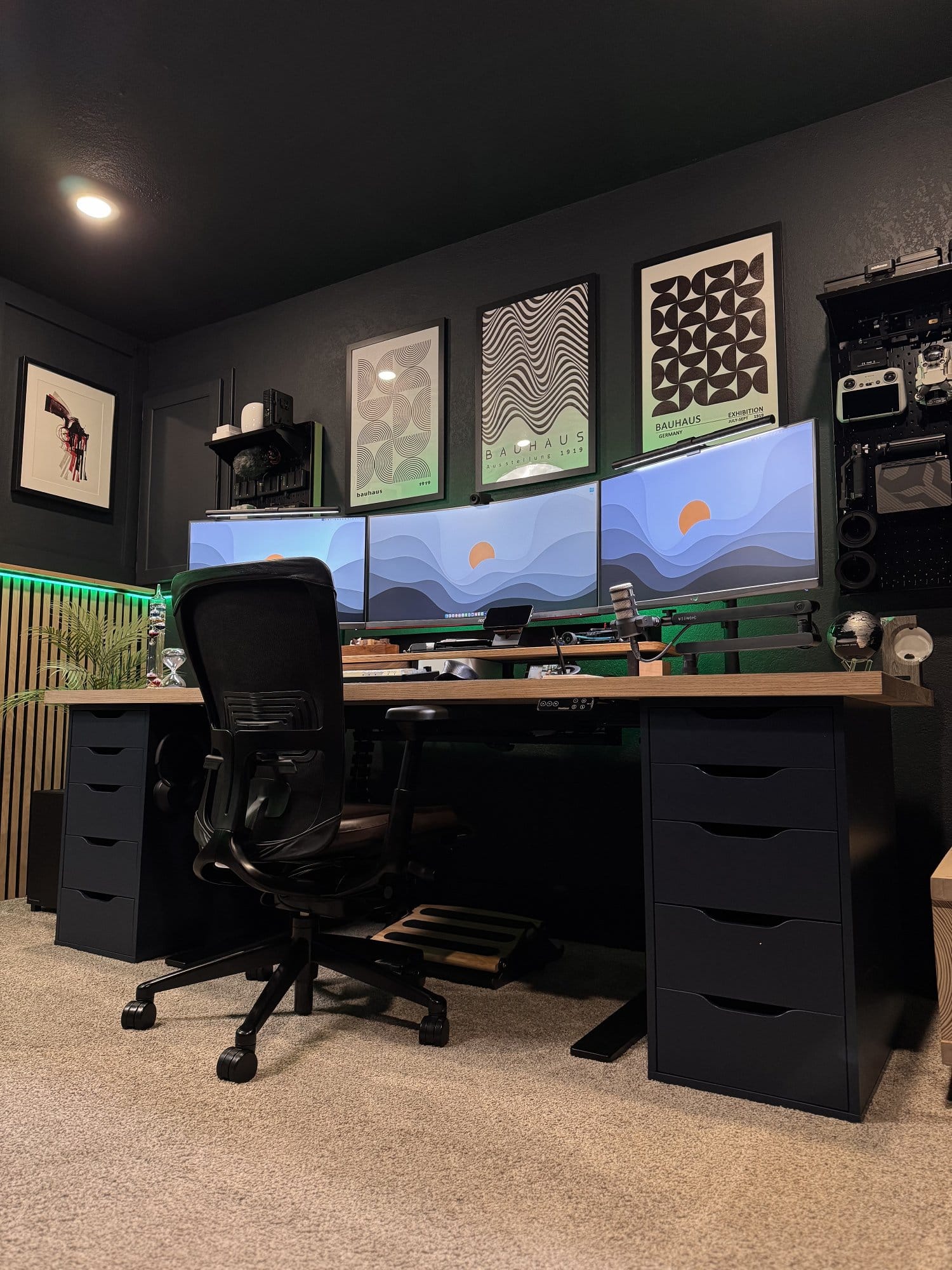 modern home office desk setup with triple ultrawide monitors, ergonomic chair, dual drawer units, wall art, and ambient green LED lighting