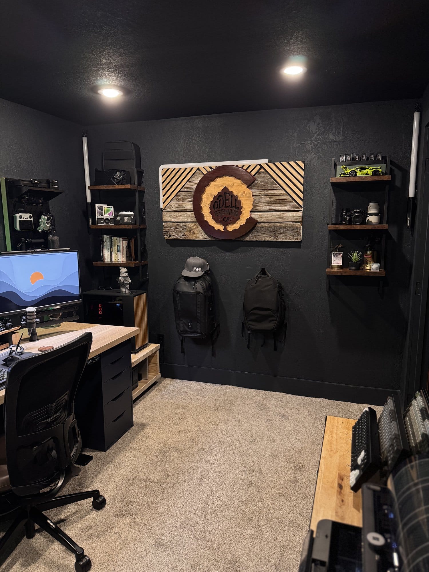 modern home office with wooden wall art centerpiece, floating shelves with books and tech gear, and a corner desk setup with monitors and ergonomic chair