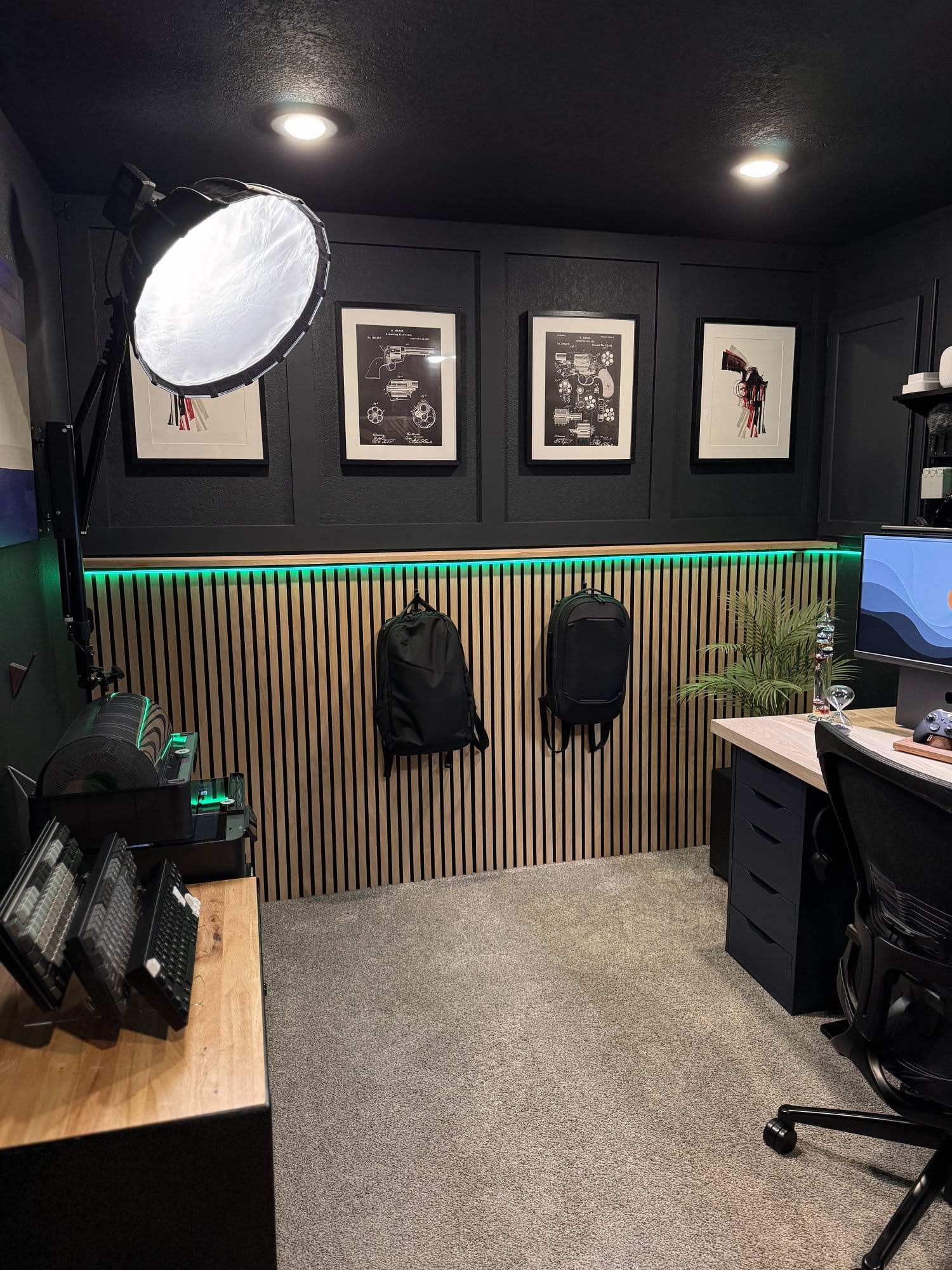 home office with acoustic wood slat wall, framed artwork, mounted backpacks, large softbox light, and modern desk setup