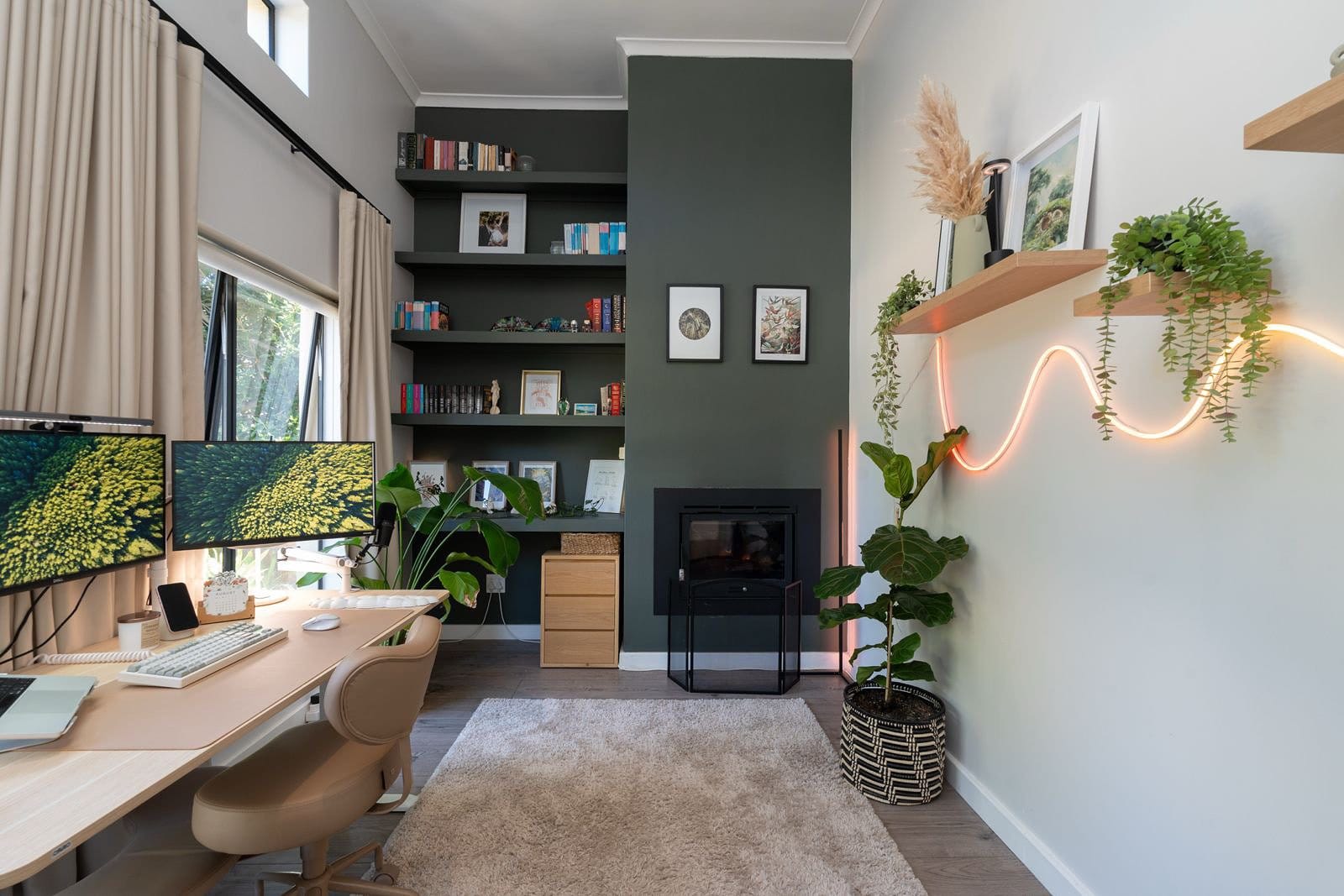 modern home office with dual monitor desk setup, meditation chair, large windows with natural light, green accent wall with built-in bookshelves, indoor plants, and cosy workspace décor