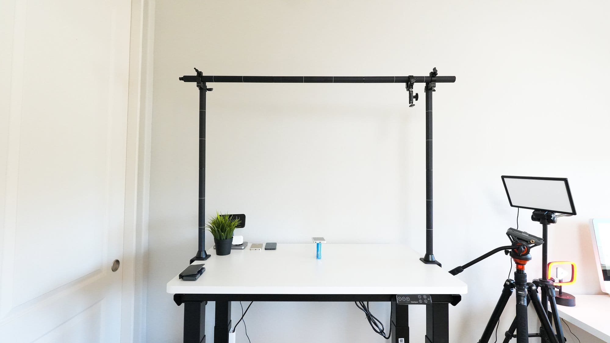 white standing desk setup with overhead camera rig, tripod lighting, and minimal accessories for filming and content creation