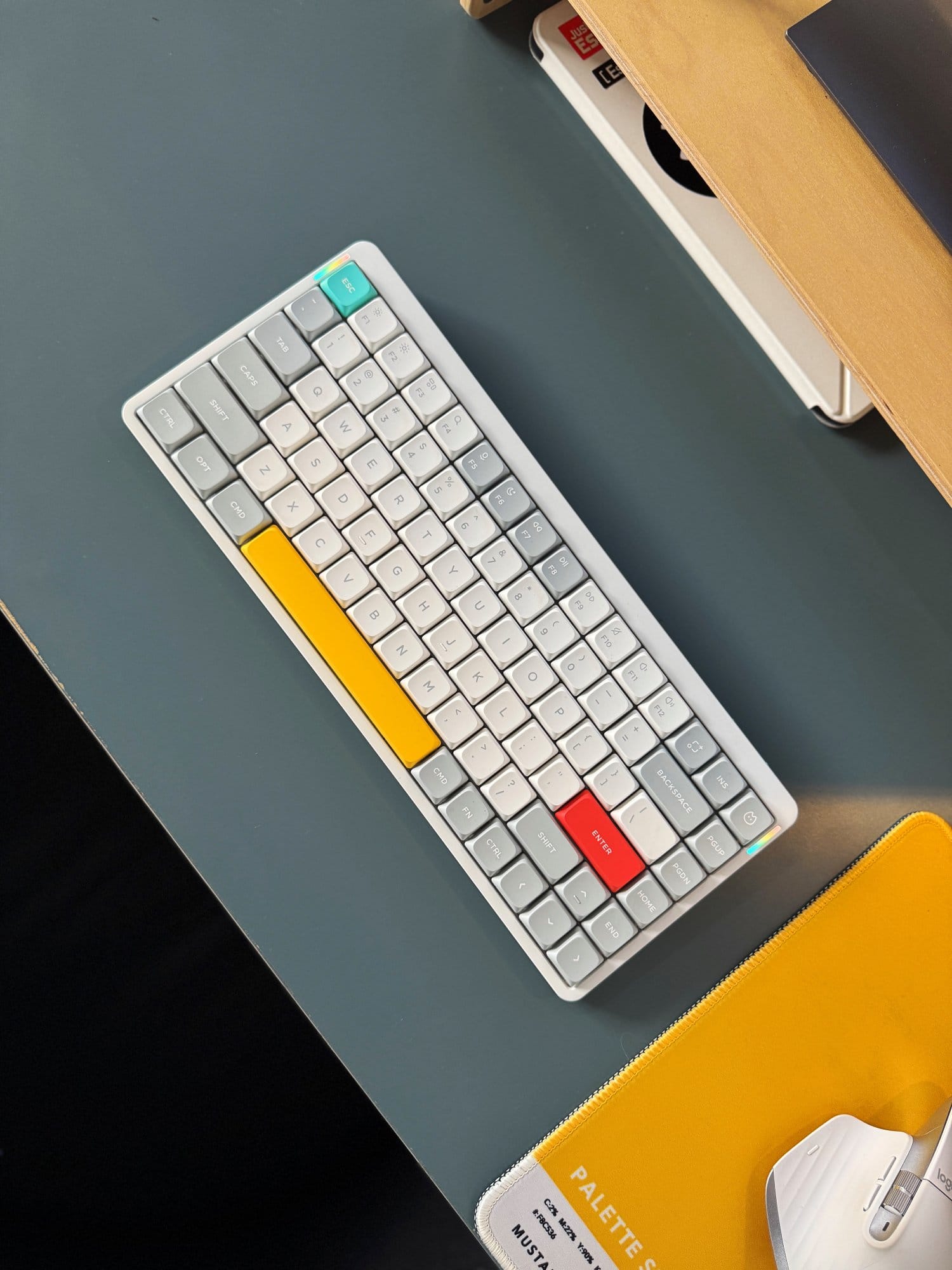 close-up of a NuPhy Air75 keyboard on a modern desk setup, featuring colourful keycaps in yellow, red, and teal beside a white ergonomic mouse and yellow desk mat