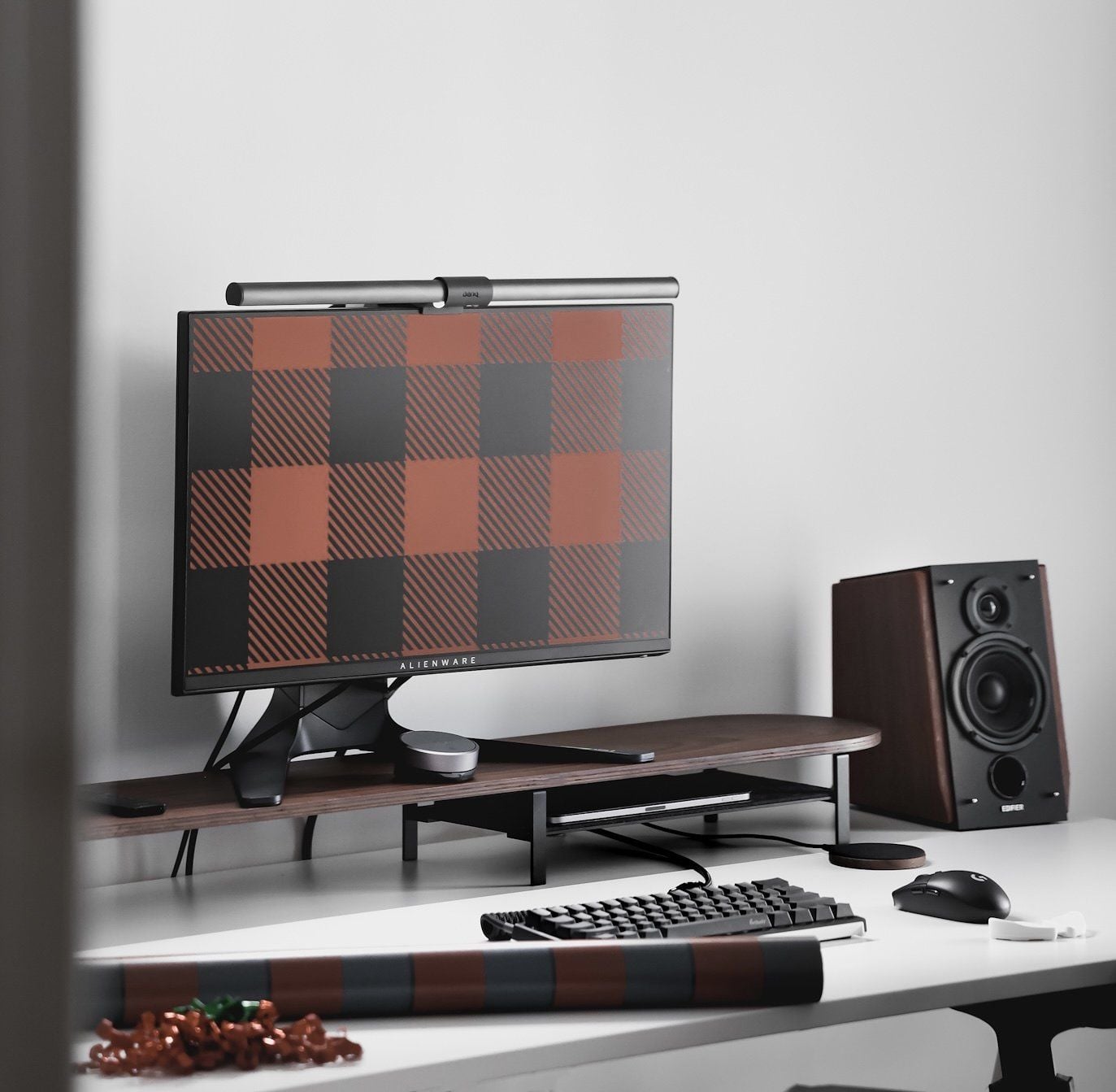 A minimal desk setup featuring an Alienware monitor with a brown check wallpaper, speakers, a mouse, and a keyboard