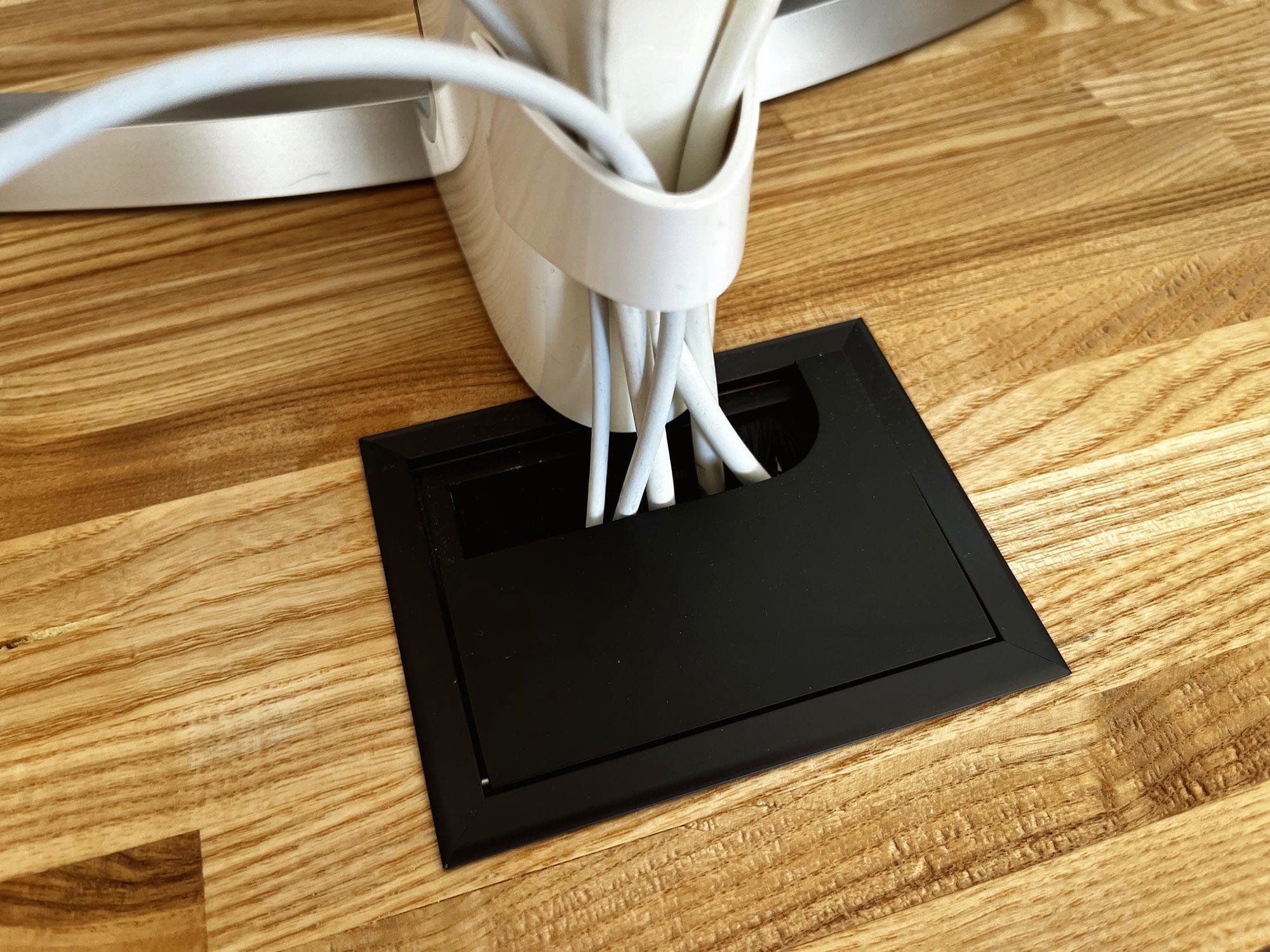 A close-up view of a cable management box on a wooden desk, organising multiple white cables from various electronic devices
