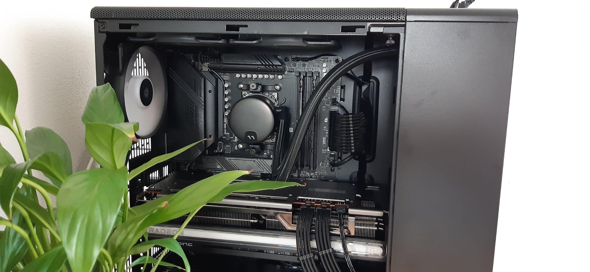 A close-up view of an open computer case showing internal components including the motherboard, cooling fan, and cables, with a green plant in the foreground