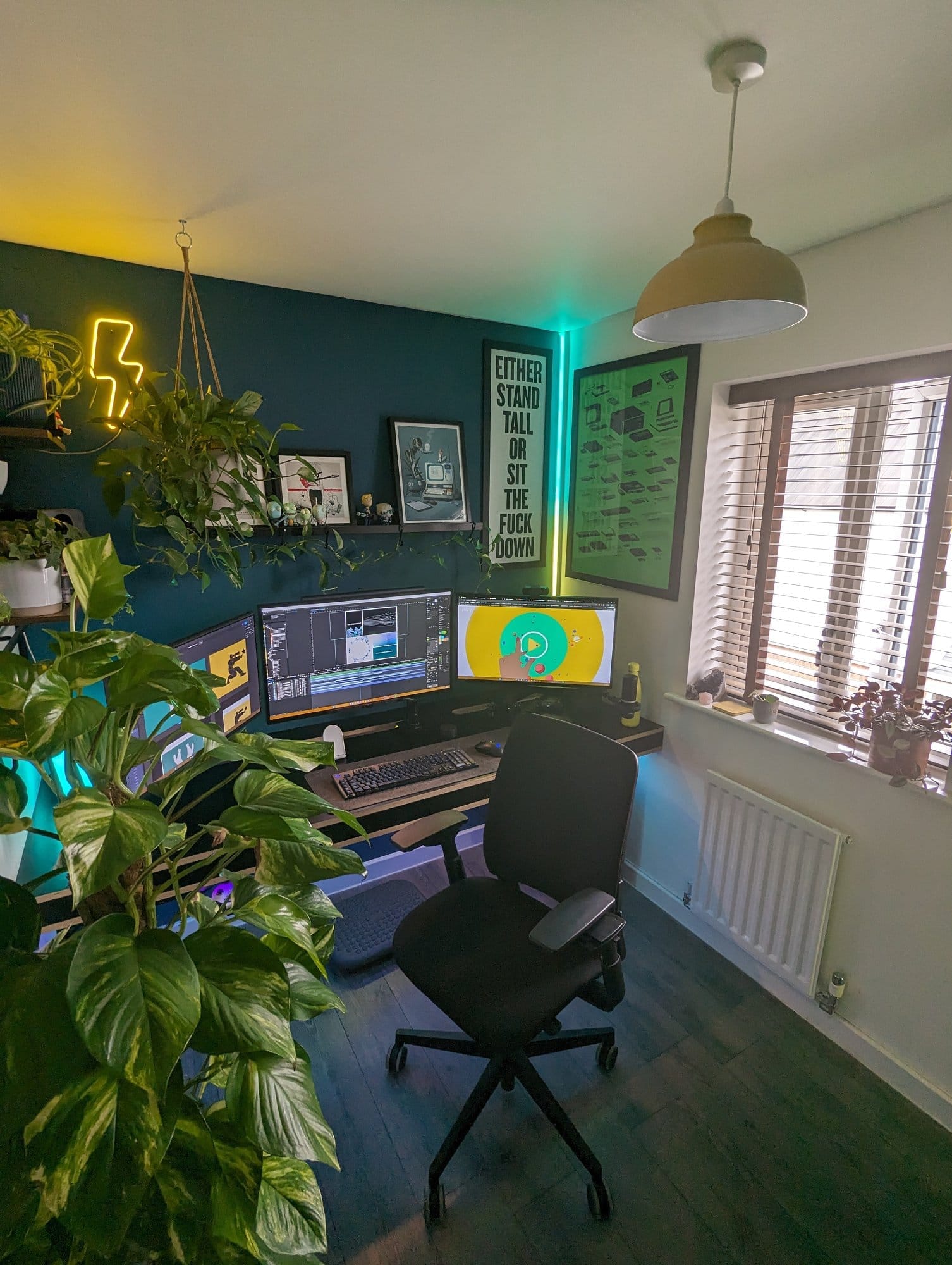 A well-organised multi-monitor desk setup in a home office with an accent deep navy wall
