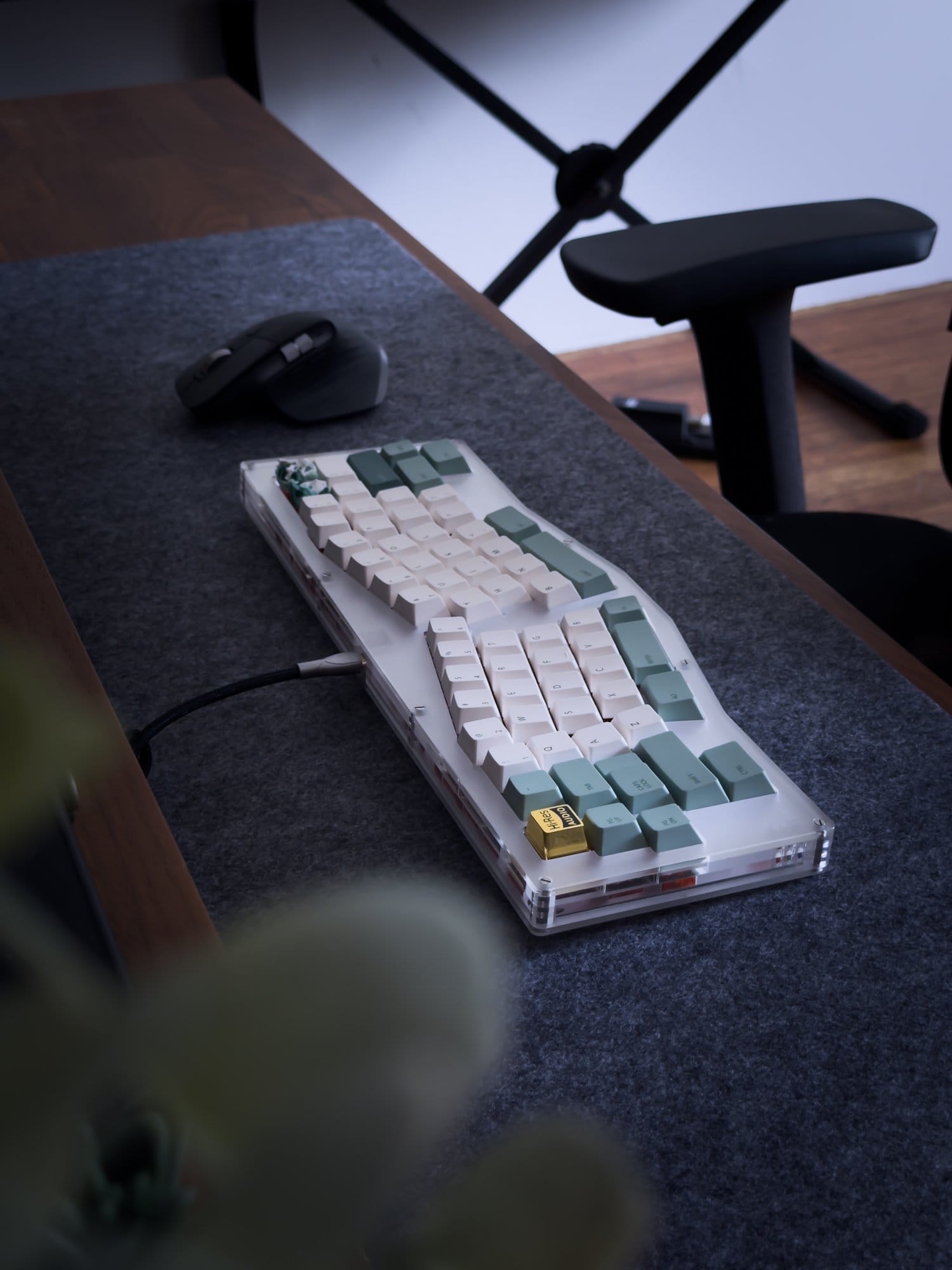 A close-up of a Switch Couture Frosted Acrylic Alice keyboard and a Logitech MX Master 3 mouse on a grey felt desk mat