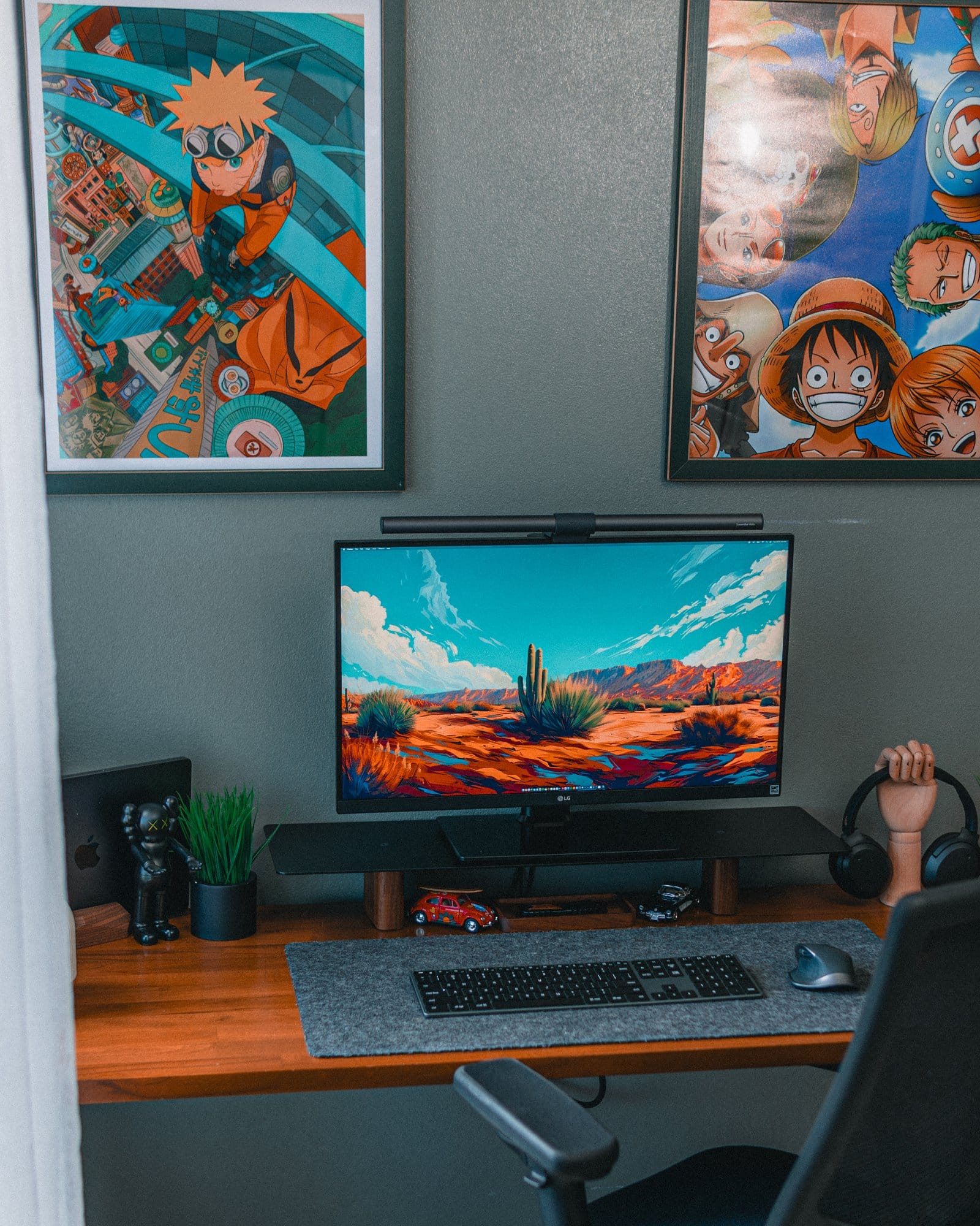 A modern desk setup, featuring an LG 27″ 27BN88U-B Ergo monitor; a BenQ Halo LightBar; a 14” M3 MacBook Pro; Edifier W820NB headphones; Edifier R1700BTS speakers; a Satechi Slim X3 keyboard; a Logitech MX Master 2S mouse; and a Hexcal desk mat. The setup is complemented by anime posters of Naruto and One Piece on the wall, and various decorative items, including a small plant, a figurine, and toy cars
