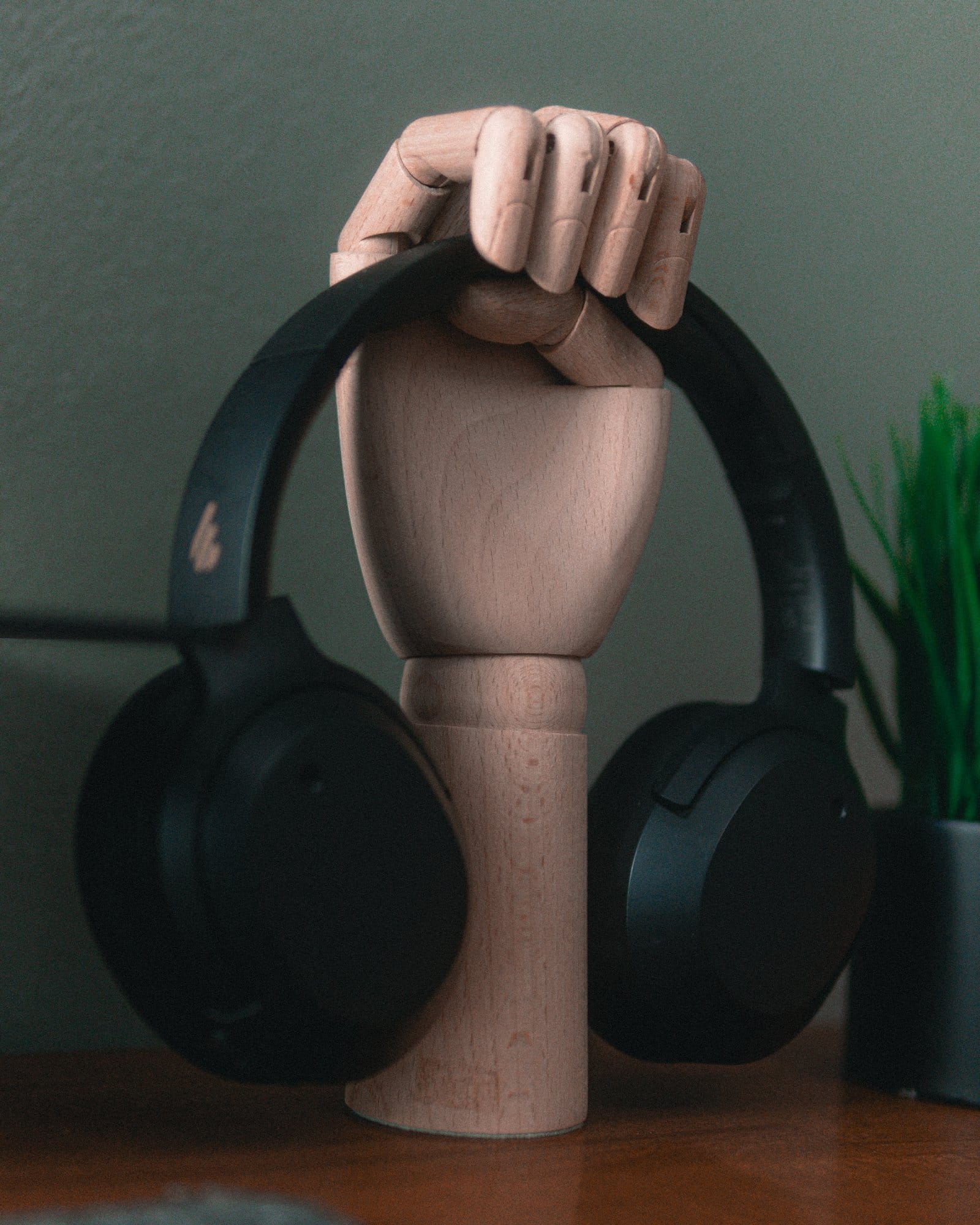 A close-up of black Edifier W820NB headphones resting on a wooden hand-shaped stand, placed on a wooden desk next to a small potted plant