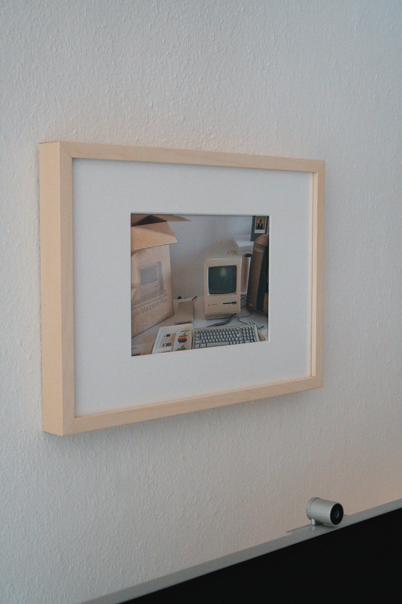 A framed picture of a vintage Apple Macintosh Plus computer setup hangs on a wall