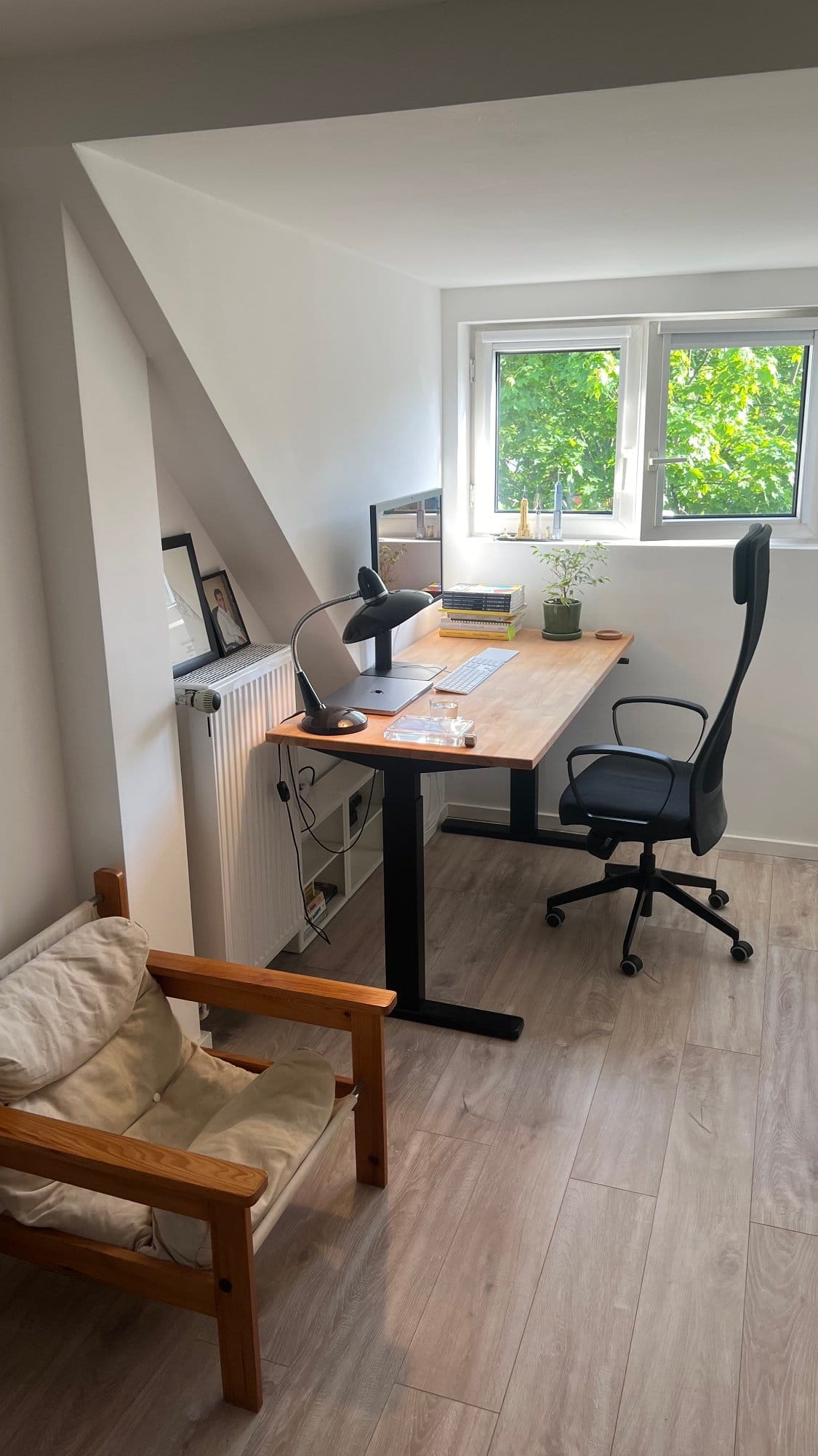 A bright and airy home office setup featuring a modern standing desk with a wooden surface, a minimalist desk lamp, a sleek office chair, and a window bringing in natural light
