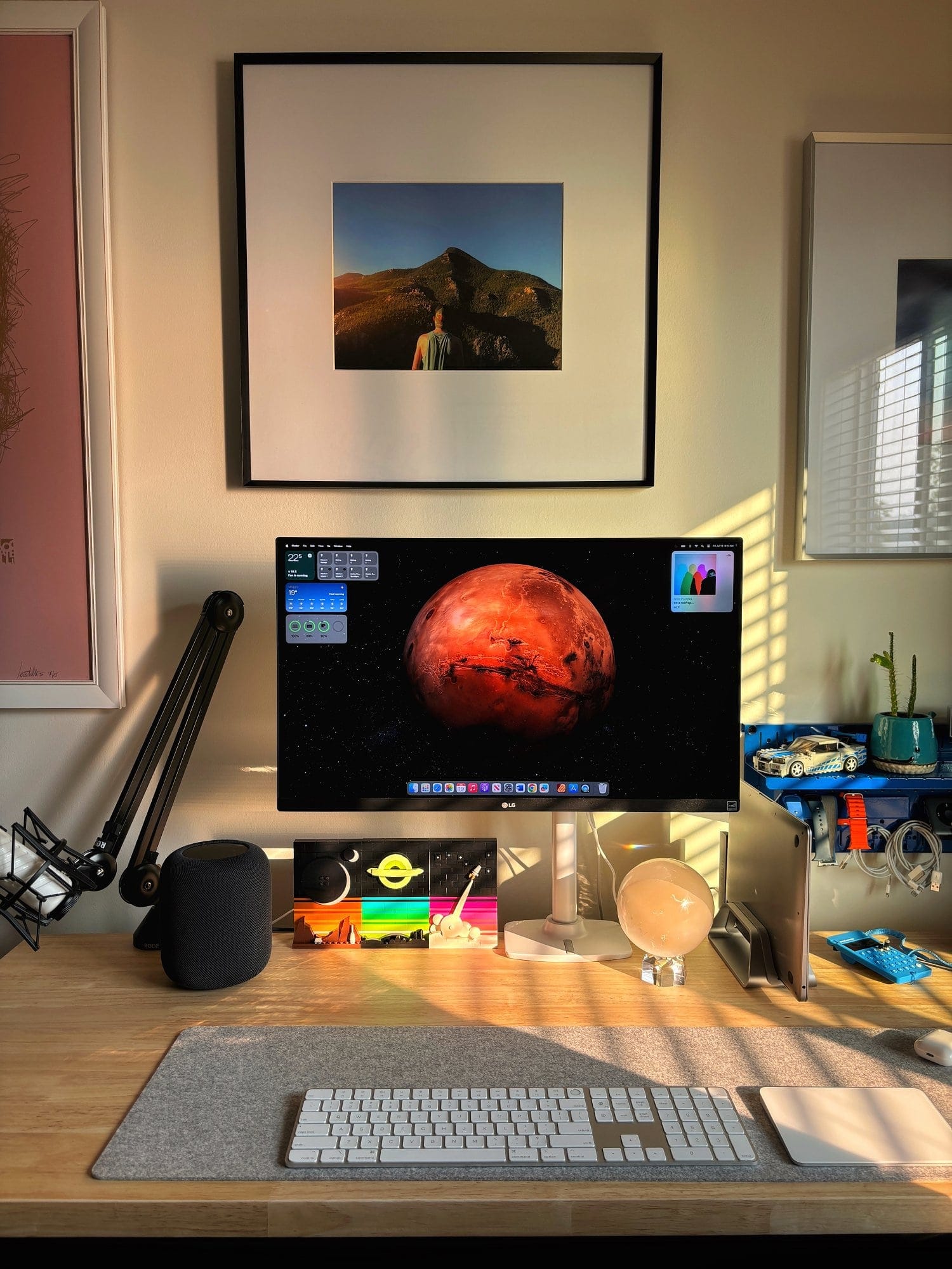 A desk setup with an LG 27″ IPS 4K UHD monitor, an Apple Magic Keyboard with Touch ID, a RØDE Podcaster microphone on a RØDE PSA1 boom arm, and a BeaverPeak Felt Desk Pad on a Husky workbench