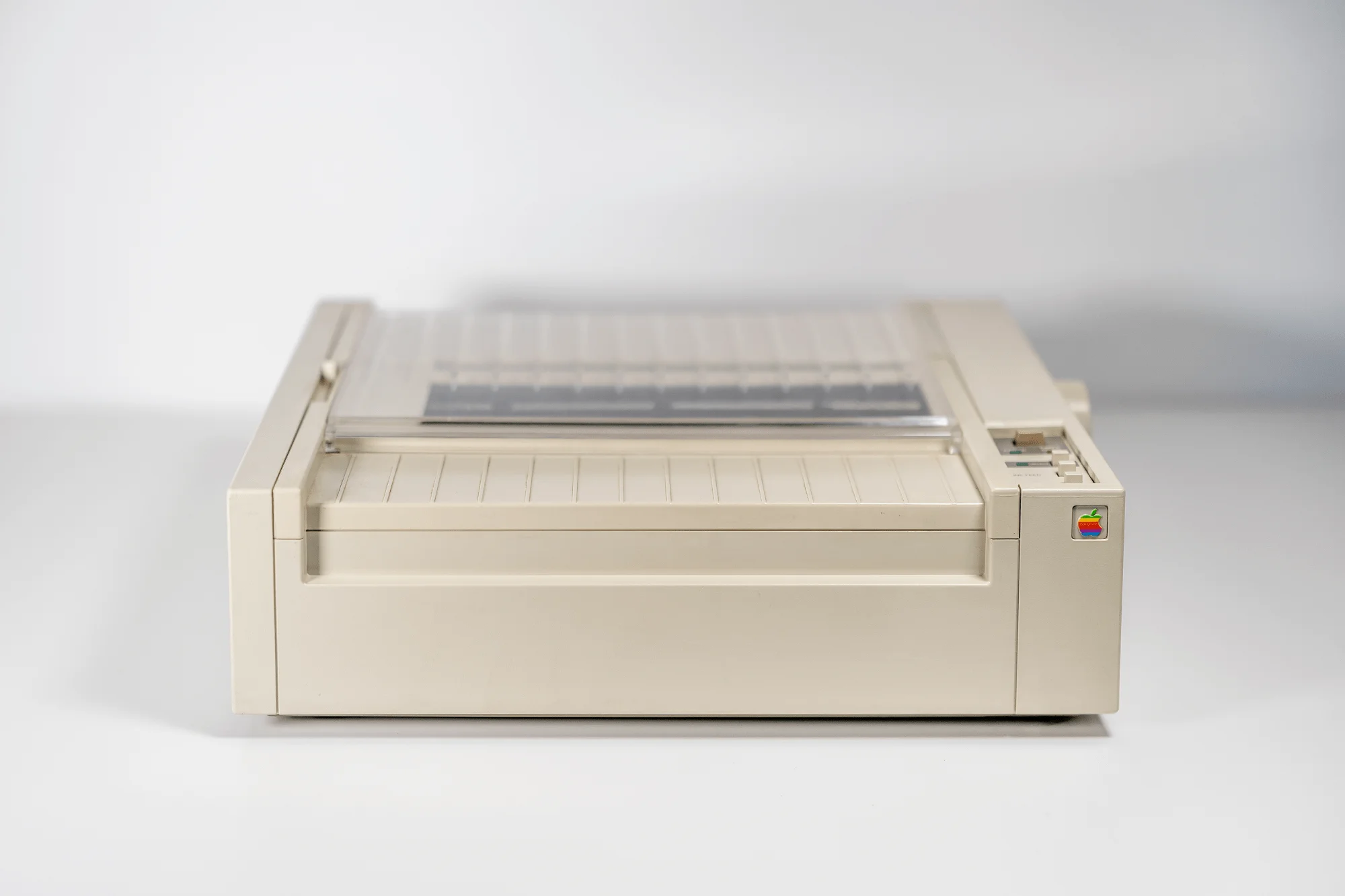 A front view of a vintage Apple ImageWriter printer on a white surface with a plain white background