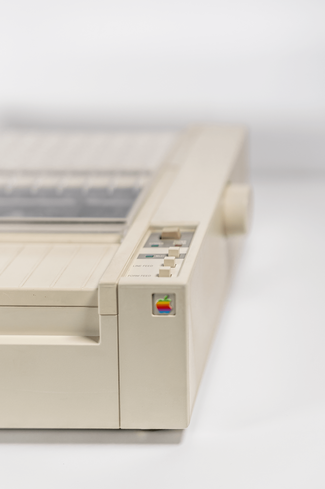 A close-up of the control panel on an Apple ImageWriter printer showing line feed and form feed buttons, with the rainbow Apple logo in the corner
