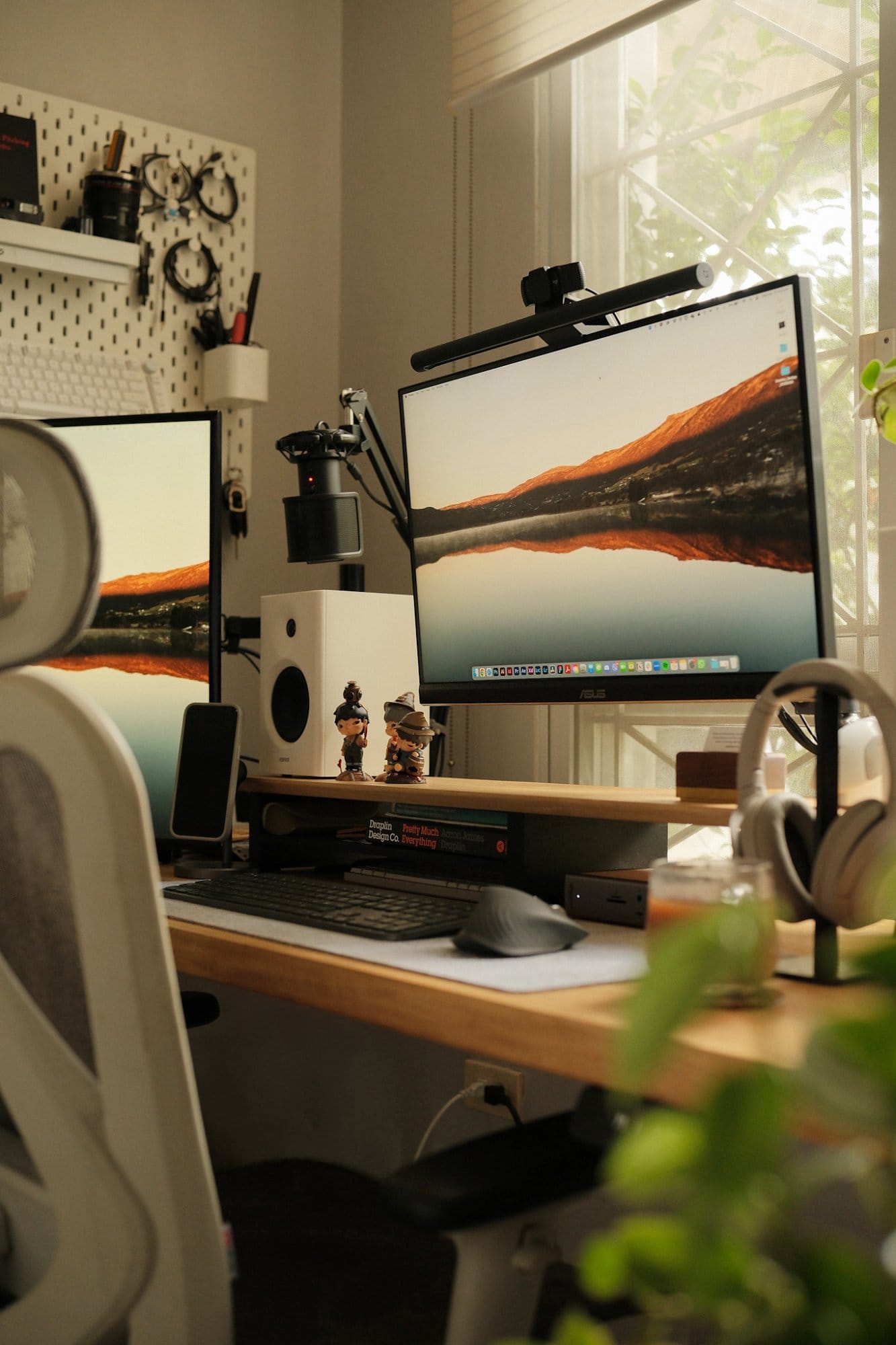 A workspace setup with an ASUS ProArt PA278QV monitor, a Samsung 1080p monitor, a Logitech MX Keys keyboard, a Logitech MX Master 3S mouse, Edifier MR4 speakers, and Sony XM4 headphones on a wooden desk beside a pegboard wall