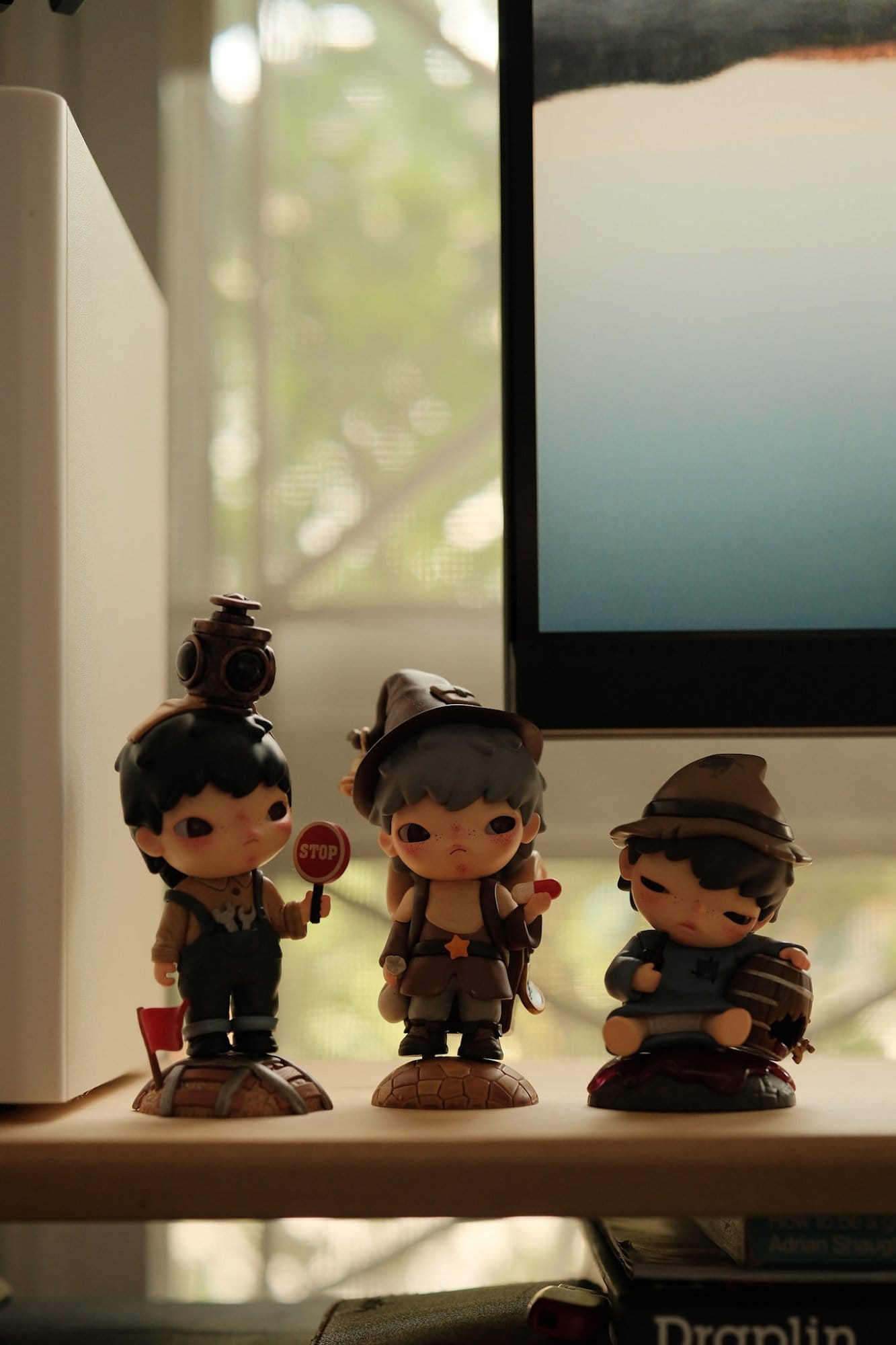 Three small figurines of cartoon-style children in explorer outfits are arranged on a desk shelf beside an ASUS ProArt PA278QV monitor and an Edifier MR4 speaker