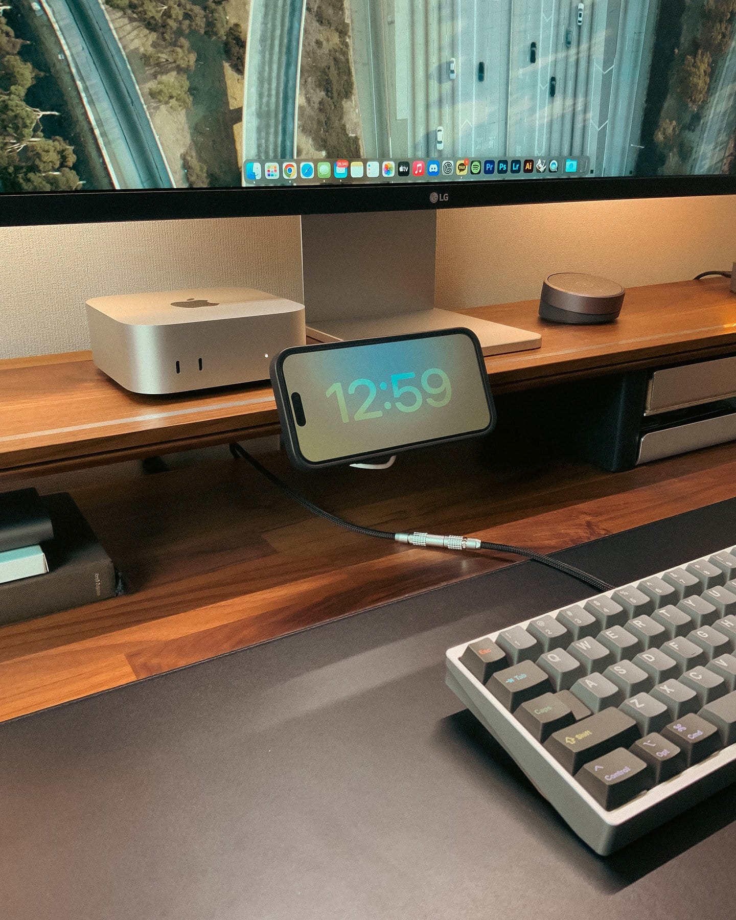 A desk shelf with a Mac Mini M4, LG monitor, iPhone on charger, and custom mechanical keyboard