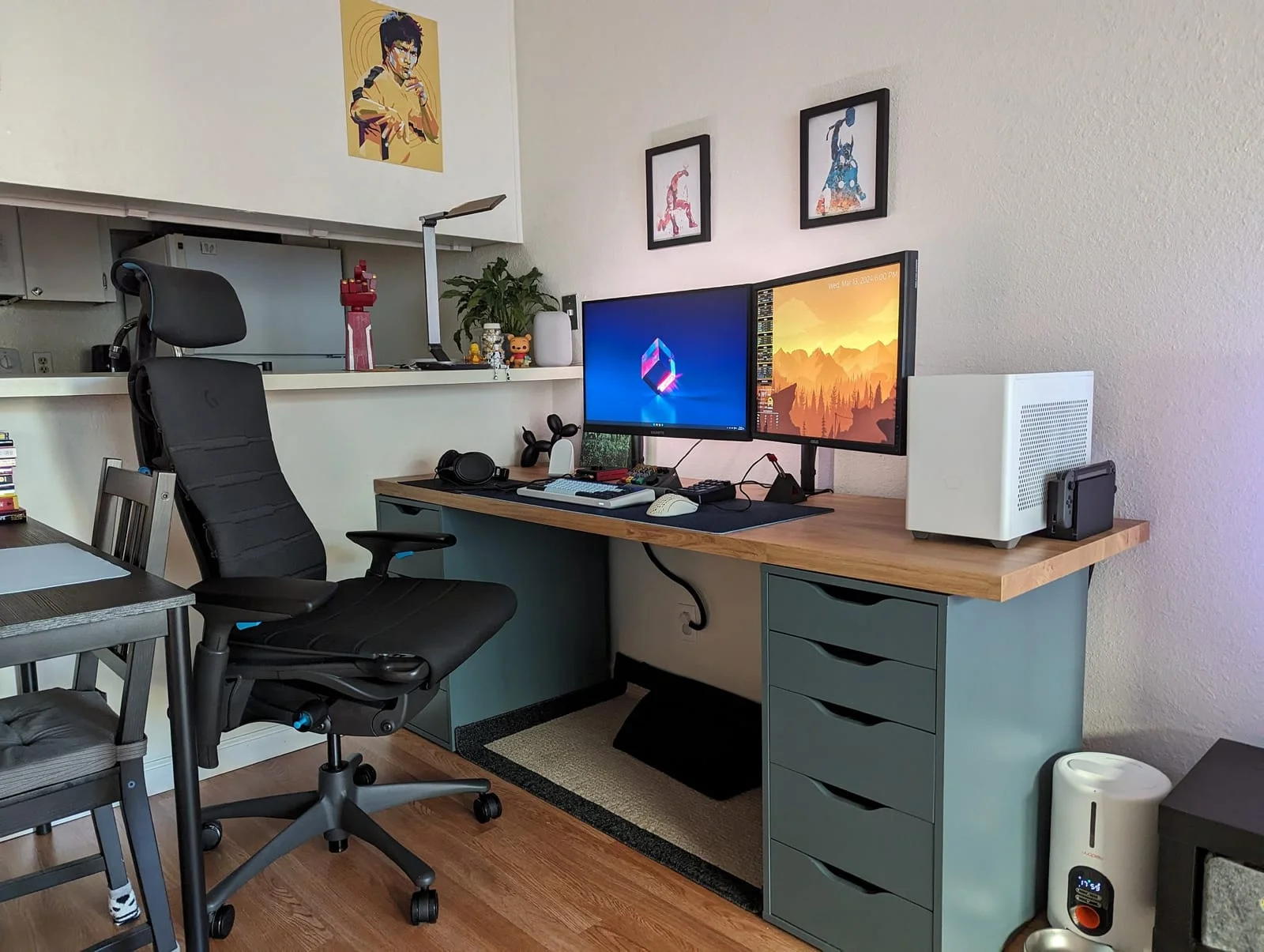 A dual-monitor desk setup with a black Herman Miller X Logitech G Embody chair and a compact white PC