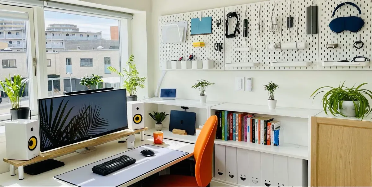 A bright home office with an ultrawide monitor, pegboard wall, and orange chair