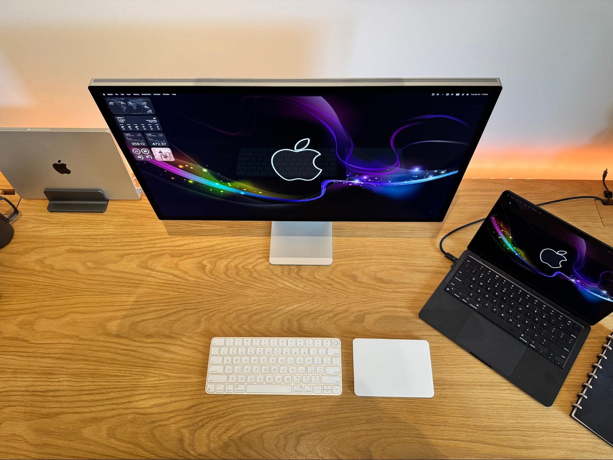 A top-down view of a desk setup with an Apple Studio Display, a MacBook Air M4, and an Apple Magic Trackpad