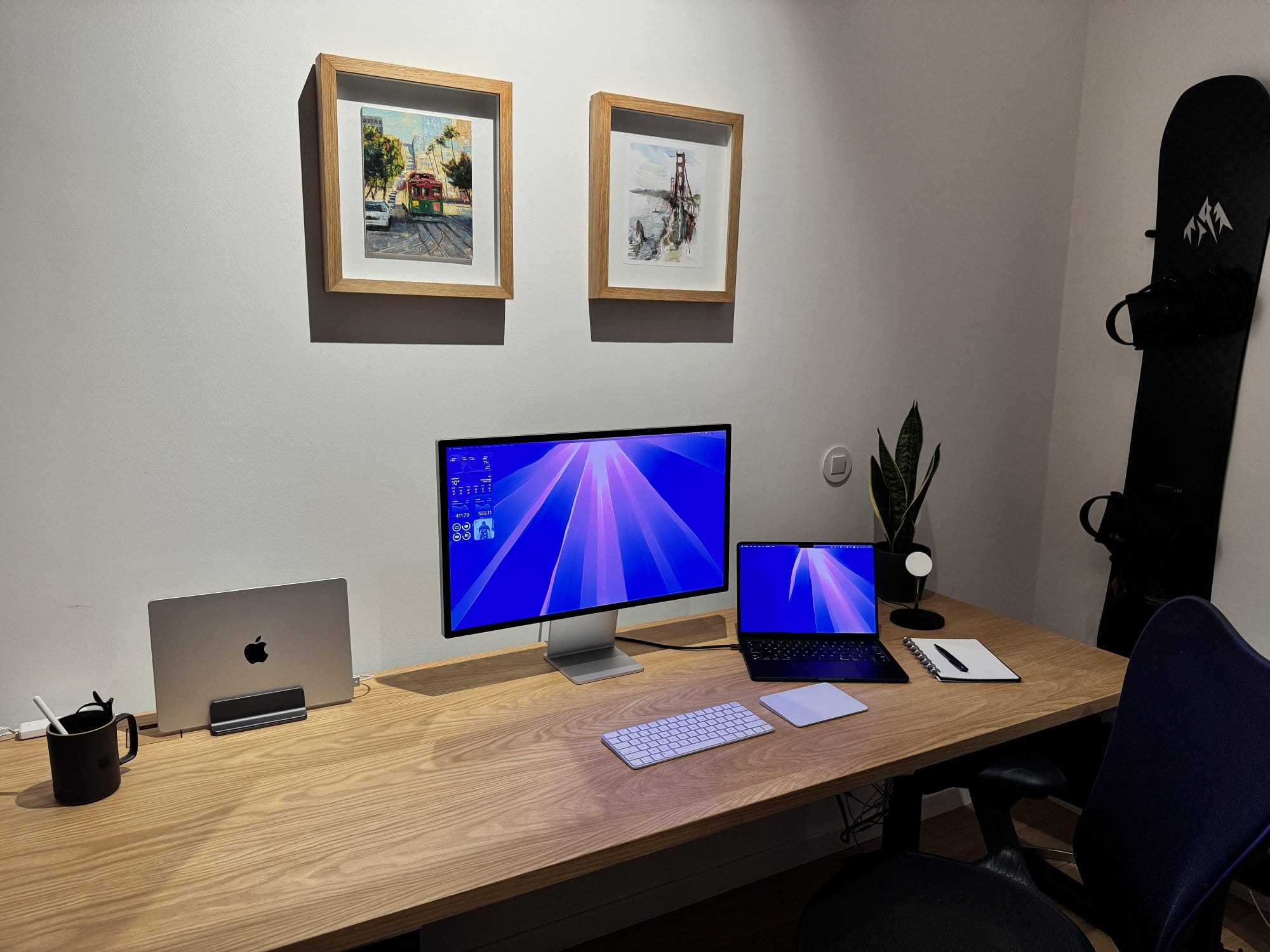 A desk setup with an Apple Studio Display, a MacBook Air M4, and a Herman Miller Aeron chair under framed prints