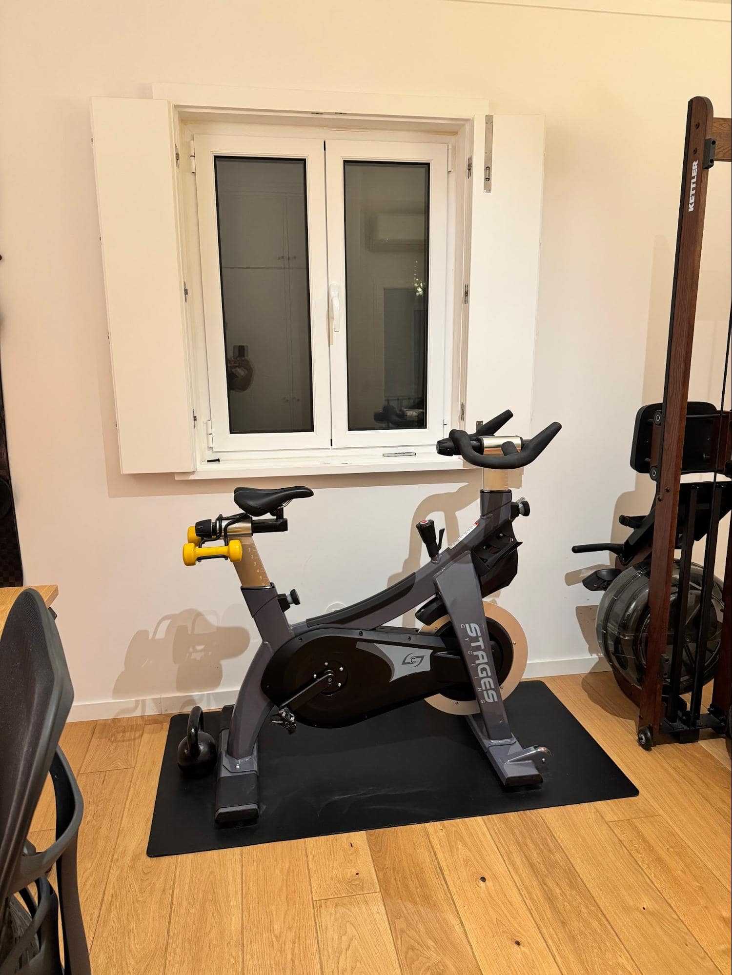 A home workout area with a Stages indoor bike, a kettlebell, and a rowing machine