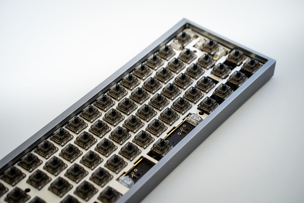 A close-up of a custom 60% mechanical keyboard build with black switches and no keycaps installed