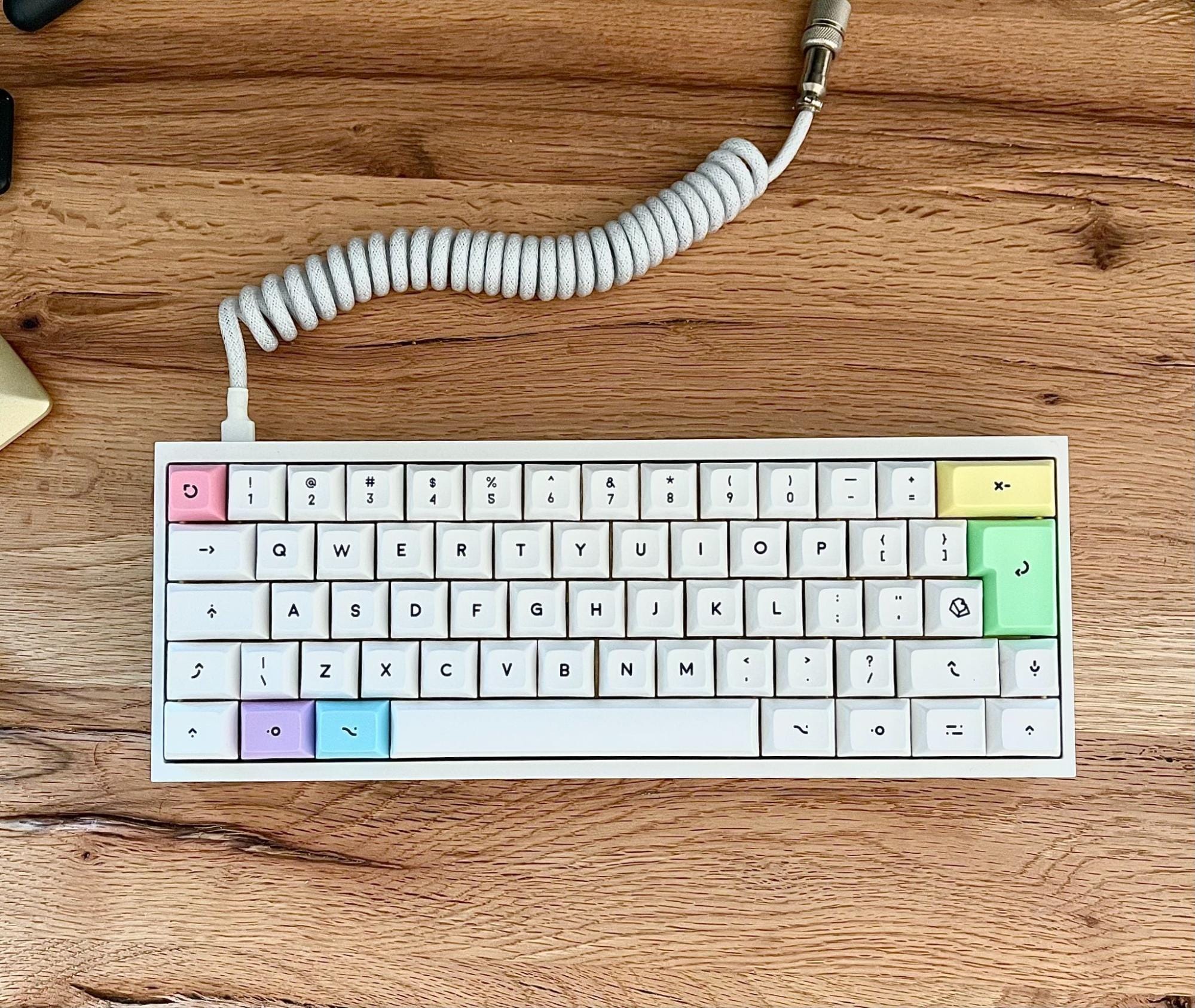 A custom 60% mechanical keyboard with PBT Cherry Milkshake keycaps and a coiled white cable on a wooden desk