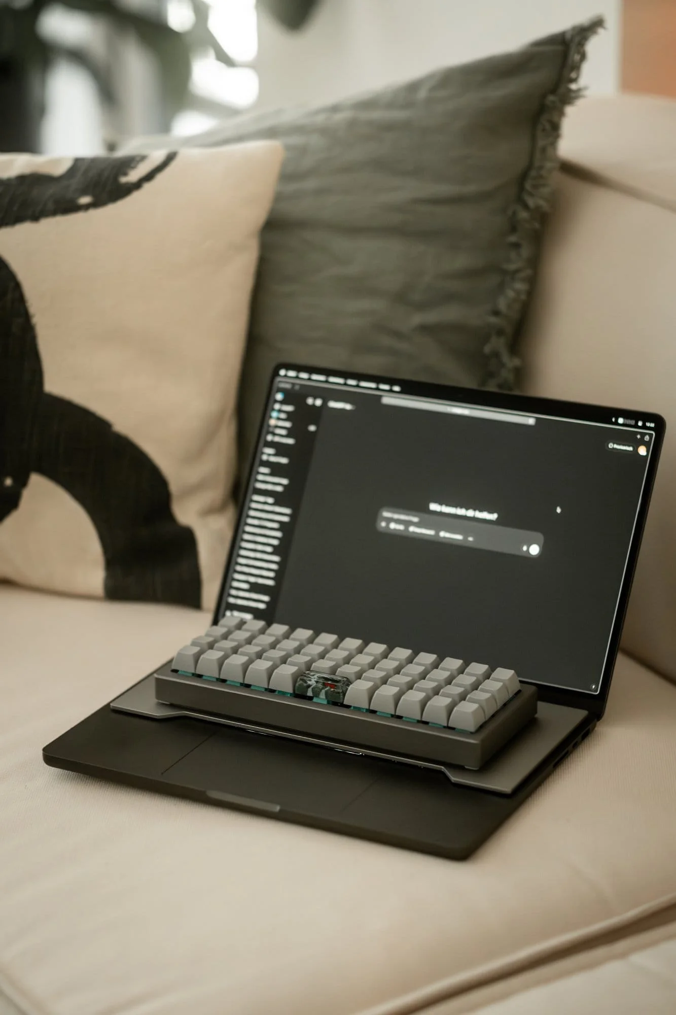 A MacBook Pro with OLKB Planck keyboard on a beige sofa