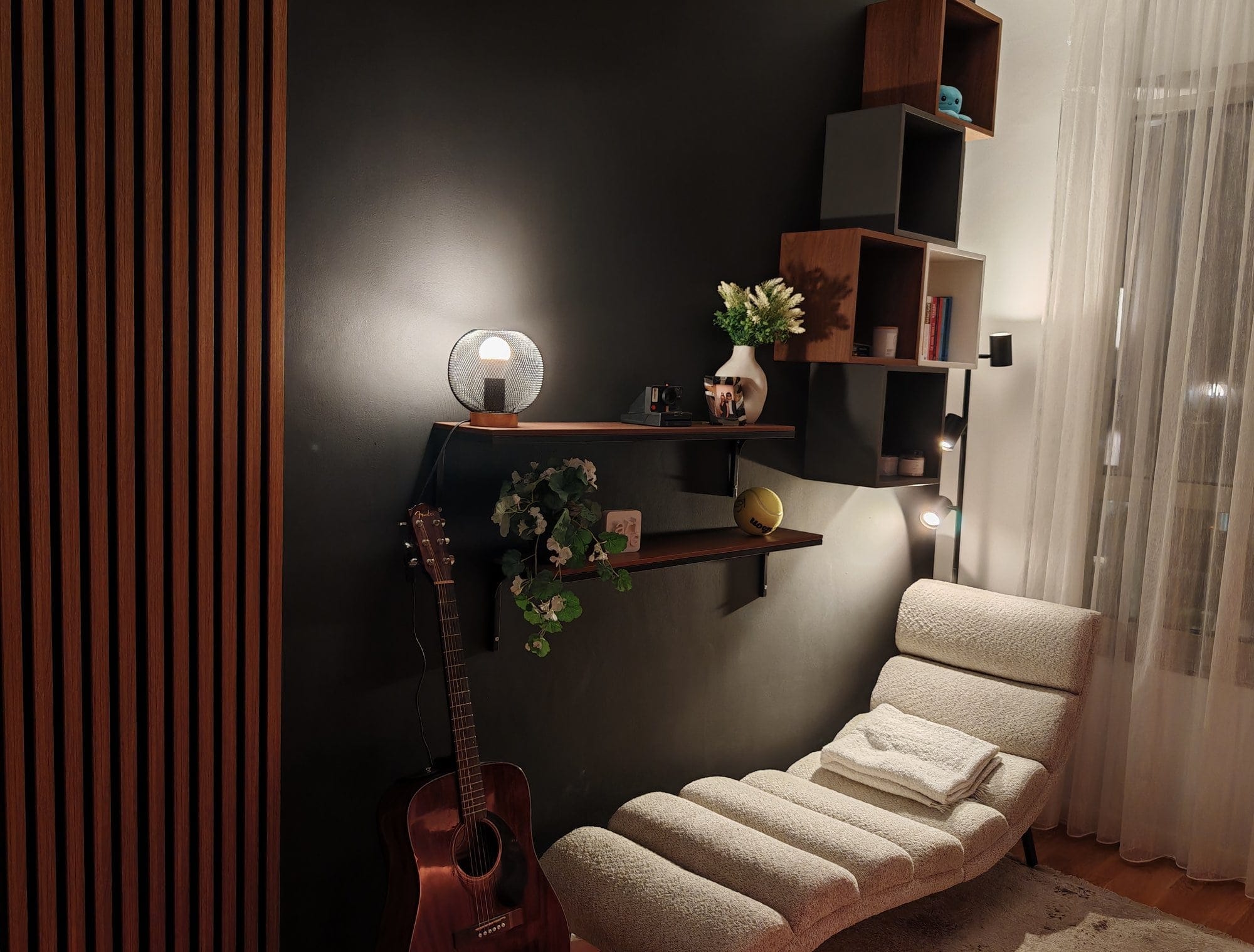 A chaise lounge under cube shelves with guitar against a black wall