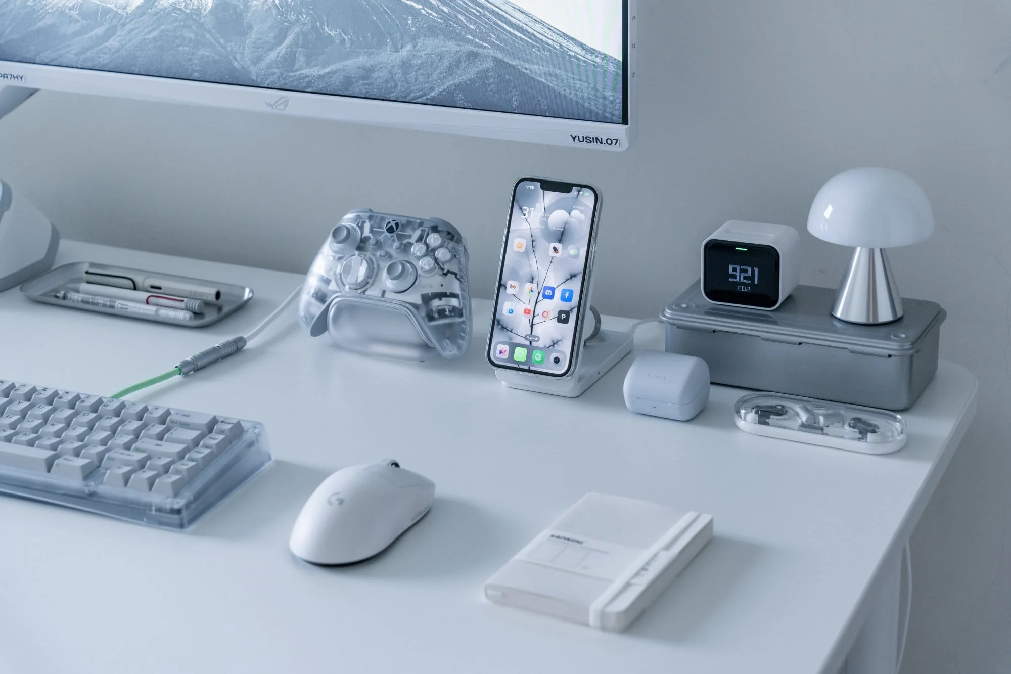 A desk with a transparent Xbox Ghost Cipher controller, iPhone on a UGREEN wireless charger and Lexon mushroom lamp