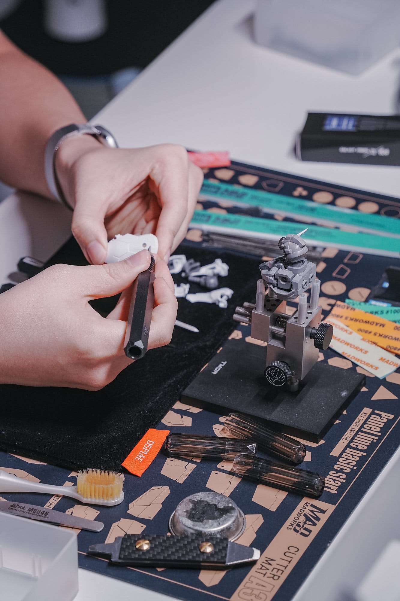 A close-up photo of hands assembling a Gundam plastic model torso in a clamp on a Madworks cutter mat